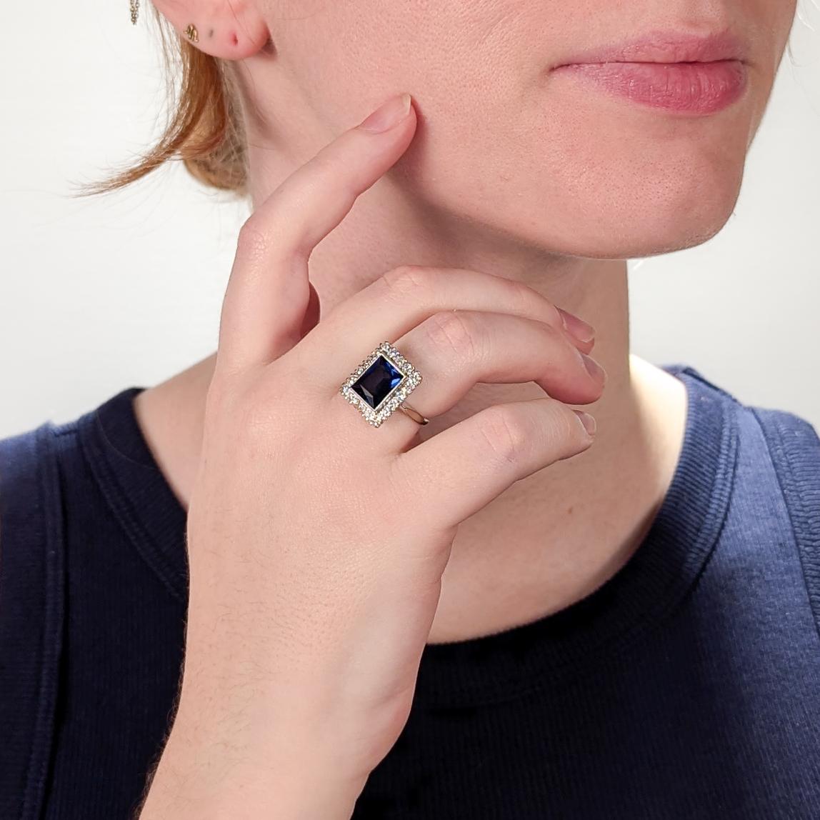 A fine vintage white gold, sapphire, and diamond ring.

In 14 karat white gold.

With a central bezel-set rectangular ca. 2.80± ct. modified brilliant cut lab-created sapphire surrounded by a halo of 18 single cut diamonds.

Marked to the