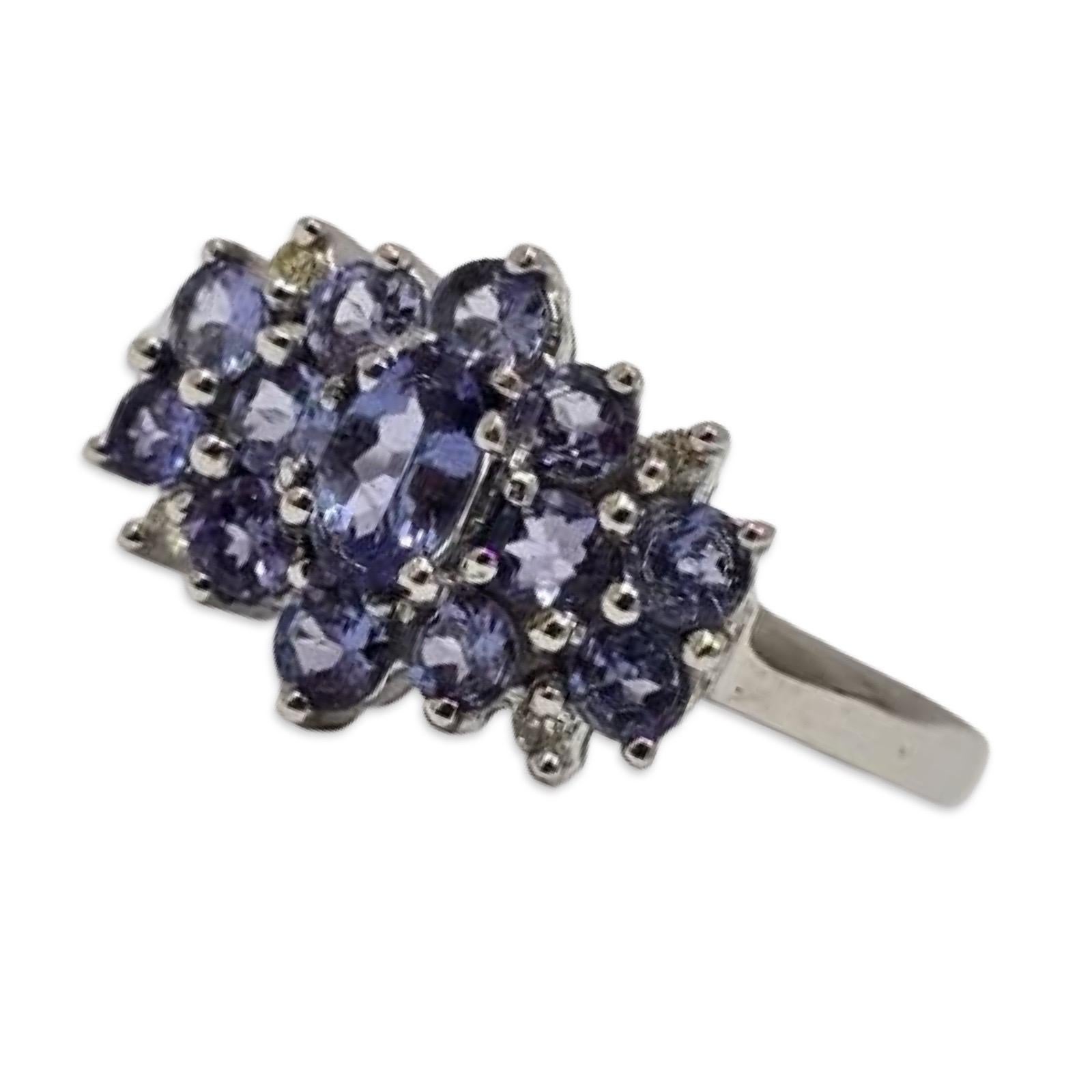 Un vibrante anello vintage in oro bianco 14K con tanzaniti naturali che rientrano nella gamma tanzanite/acquamarina del Presidium Gem Tester. La tanzanite ovale centrale misura circa 5 mm x 3,15 mm, incorniciata da dodici tanzaniti di 2,65 mm