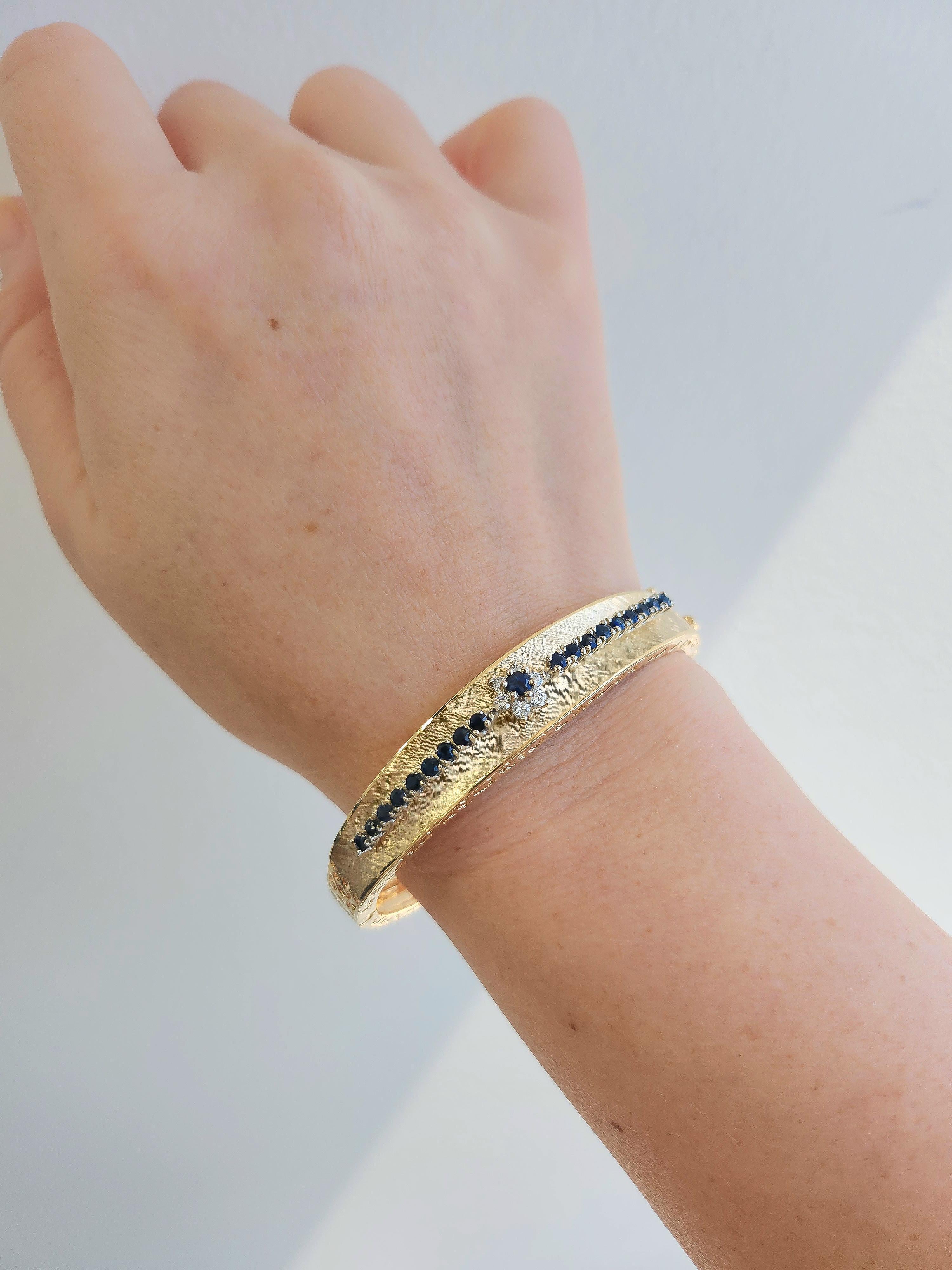 If you love vintage jewelry with charm and character, this sapphire and diamond bangle might be your next favorite piece. Crafted in solid 14K yellow gold, it features rich midnight blue sapphires, a sparkling diamond flower centerpiece, and