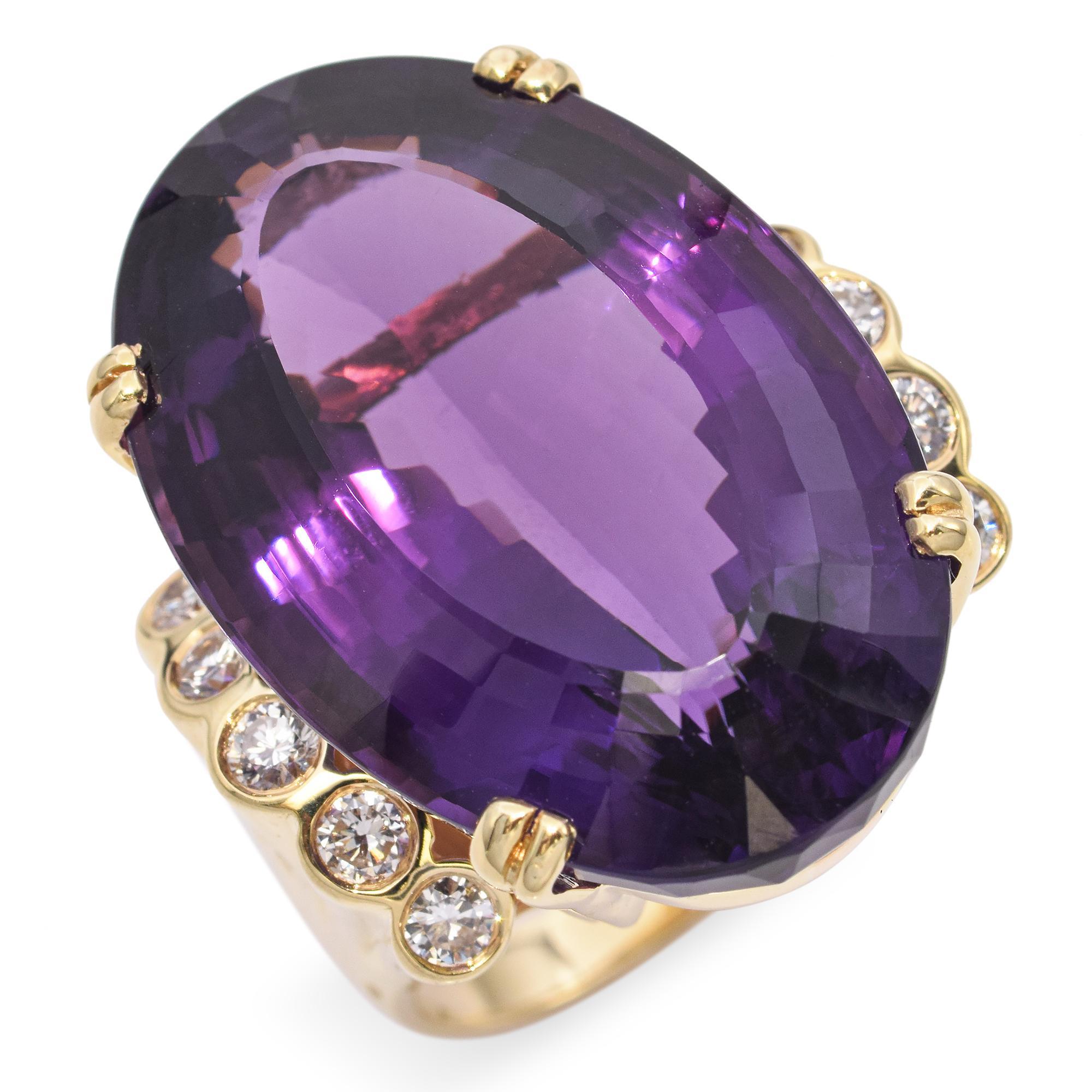Dieser auffällige Ring zeigt einen großen, facettierten ovalen Amethysten, der in 18 Karat Gelbgold gefasst ist. Der Amethyst ist von einer Reihe funkelnder Diamanten umgeben, die von goldenen Zacken gehalten werden. Der tiefe violette Farbton des