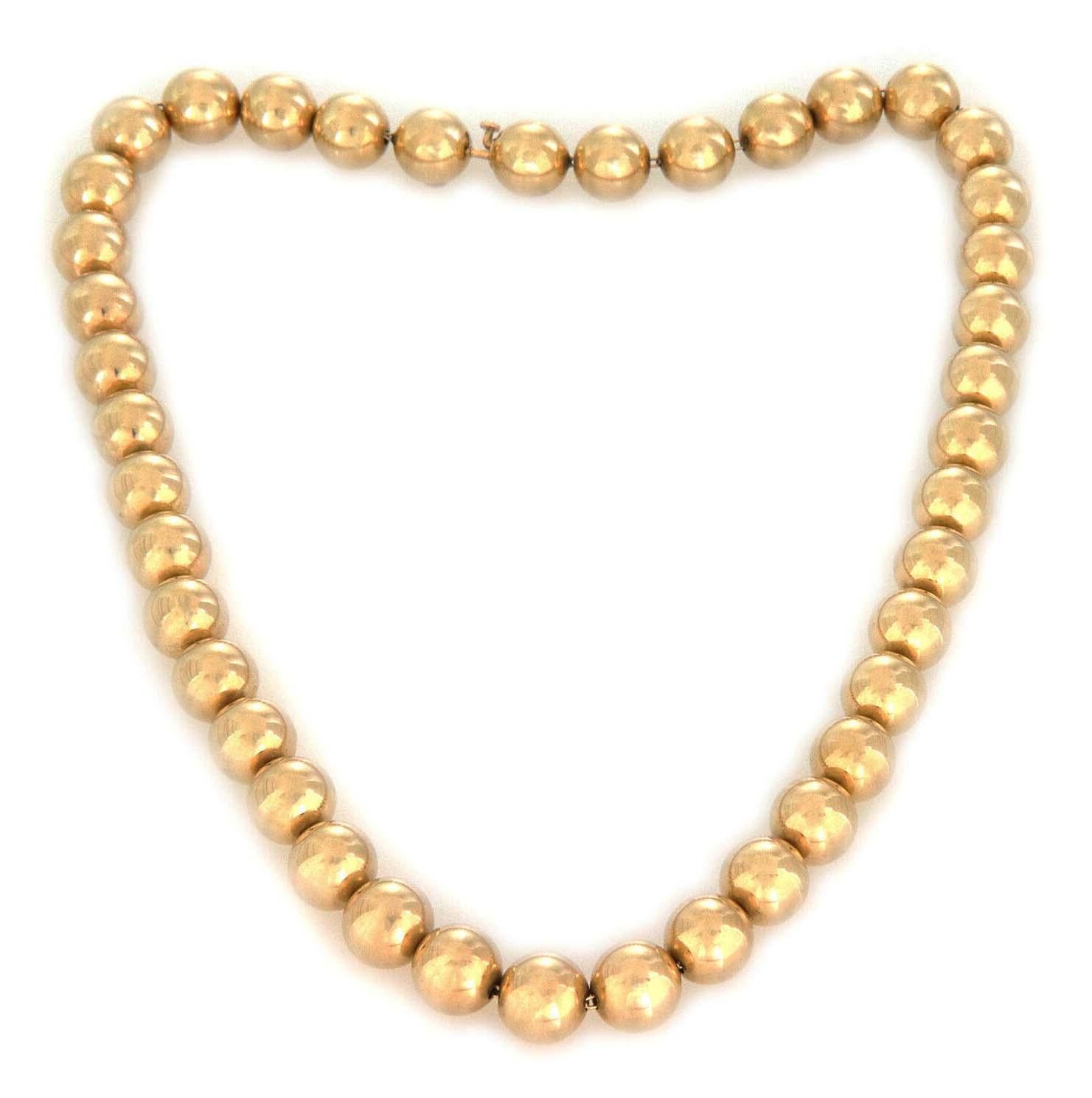 This lovely vintage necklace is crafted from 14k yellow gold. It features high polished gold beads beads strung on a slim oval link chain. The beads are 9.5mm each and the necklace secure with a slim slide clasp with the 14k gold content