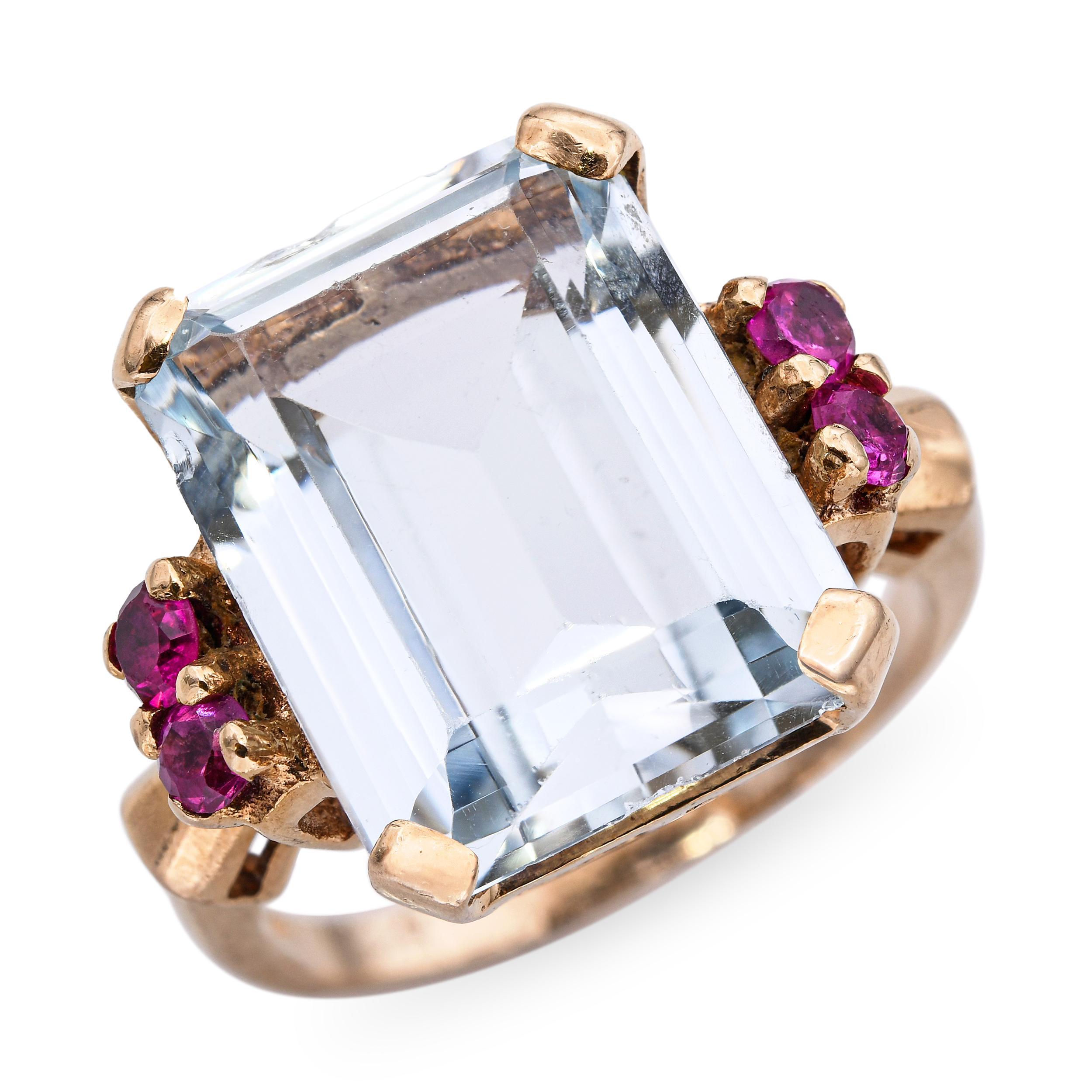 Questo anello cocktail vintage in oro giallo 14k ha al centro una splendida acquamarina da 9,95 carati, accentuata da un'aureola di rubini vibranti per un totale di 0,24 carati. Il contrasto tra il blu freddo dell'acquamarina e il rosso intenso dei
