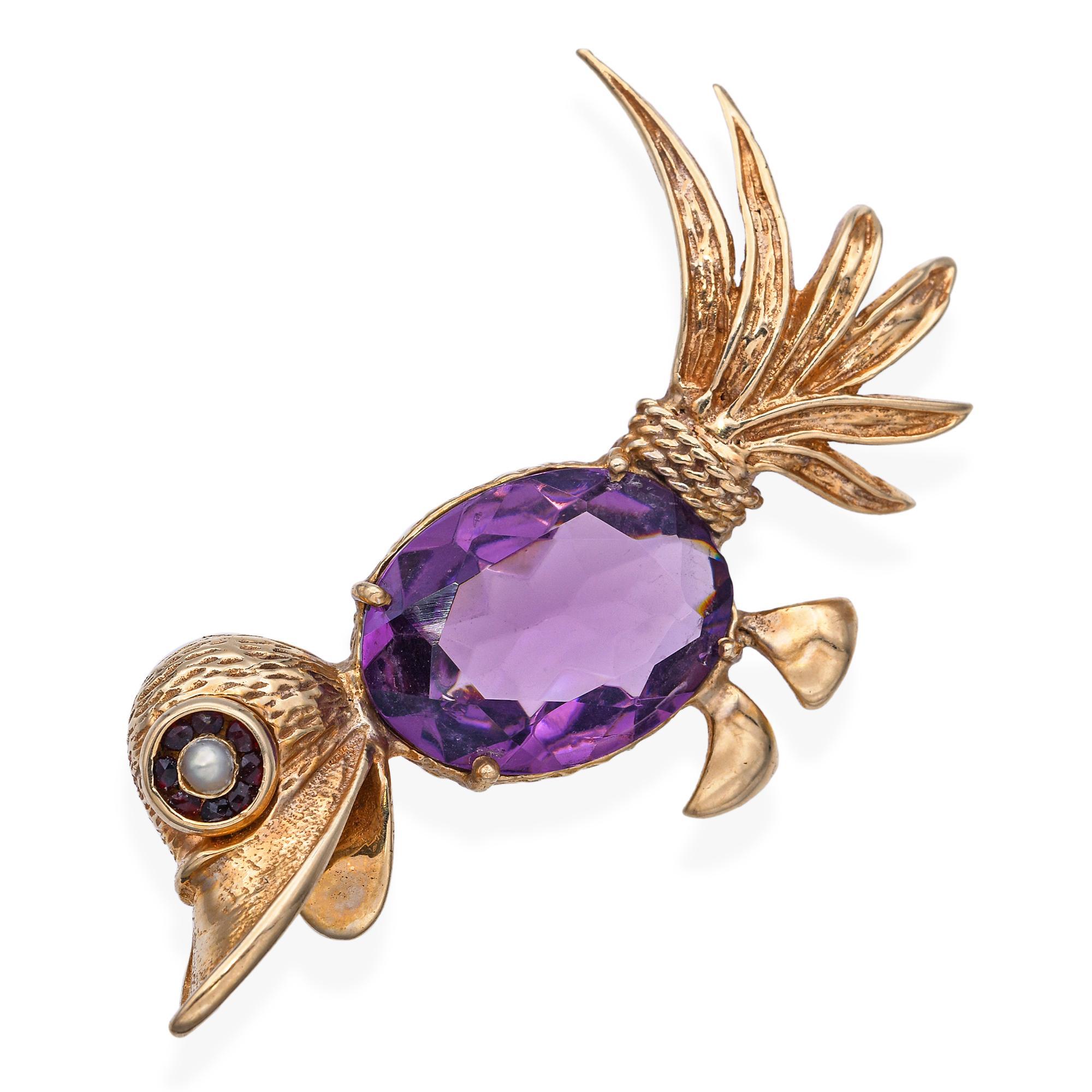 This delightful vintage bird brooch is crafted in 14k yellow gold and features a large, richly hued amethyst as the body. The eye is formed by a luminous seed pearl, encircled by a halo of deep red garnets for added brilliance and detail. Elegant