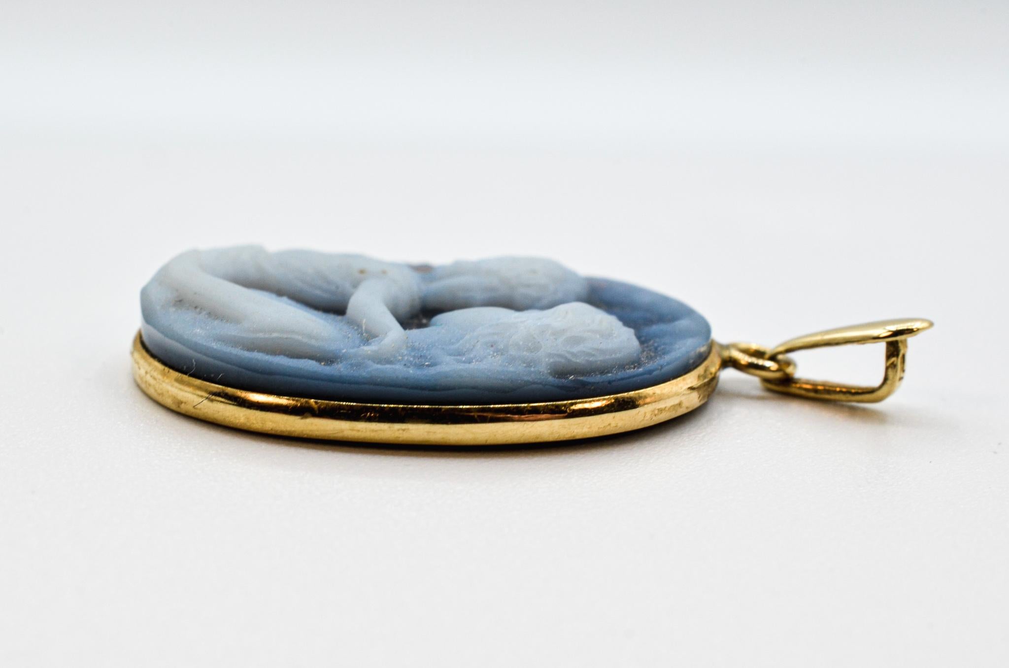 A lovely piece depicting a mother and child, a manifestation of tender love, sweetness, and devotion. This pendant features a stunning oval blue agate carved with a silhouette portrait of a mother with a child in her arms hugging her. Finished in