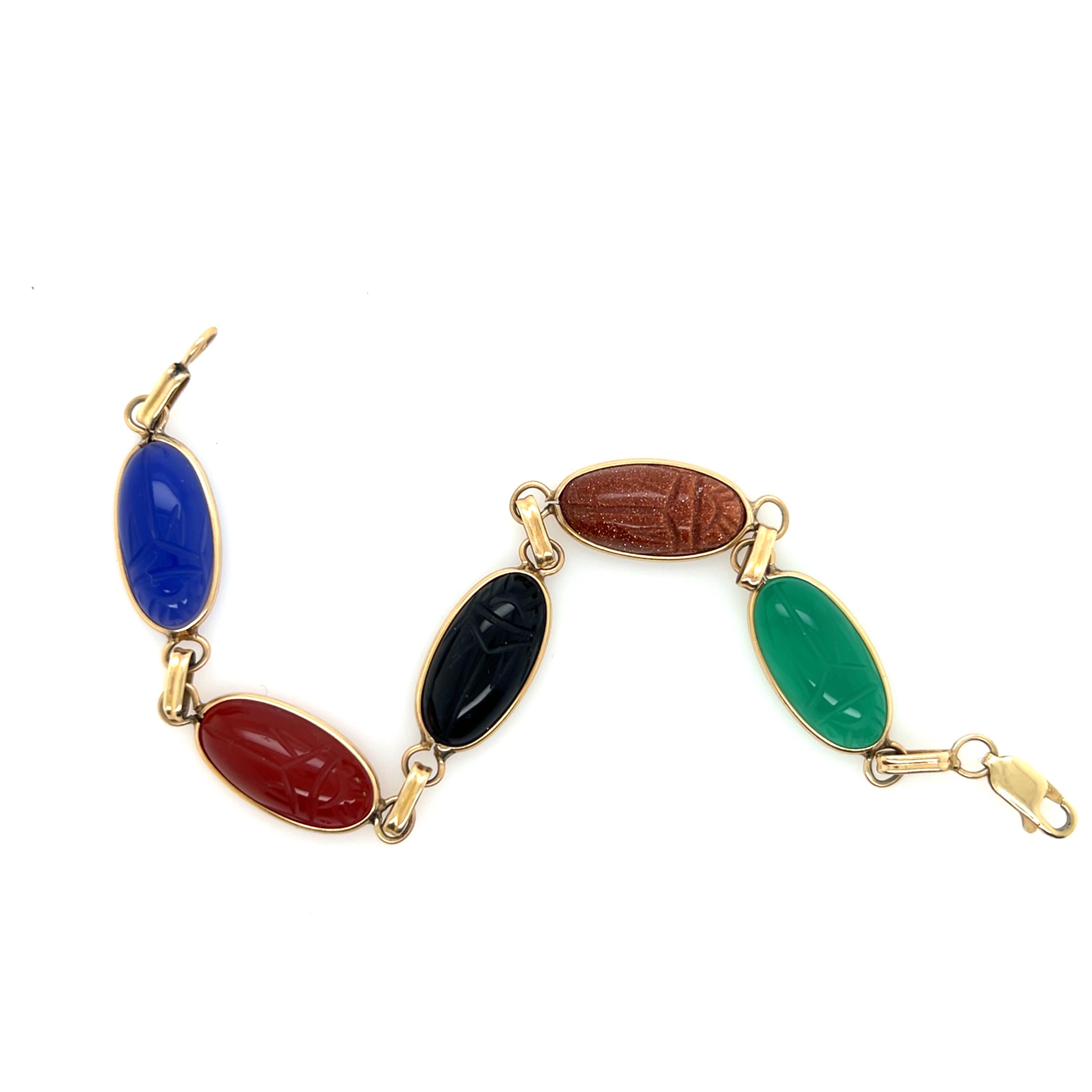 This vintage bracelet from the 1970s showcases five beautifully carved scarab gemstones set in warm 14-karat yellow gold bezels. The ancient Egyptian scarab motif, symbolizing rebirth and protection, is rendered in a stunning array of natural stones