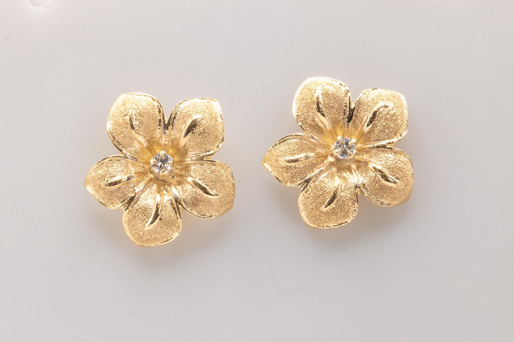 These elegant and unique 14k yellow gold earrings feature a delicate floral design, each adorned with a single round brilliant diamond of approximately 0.10 carats (G-H color, VS clarity). Weighing 5 grams and measuring 1 inch in length, these