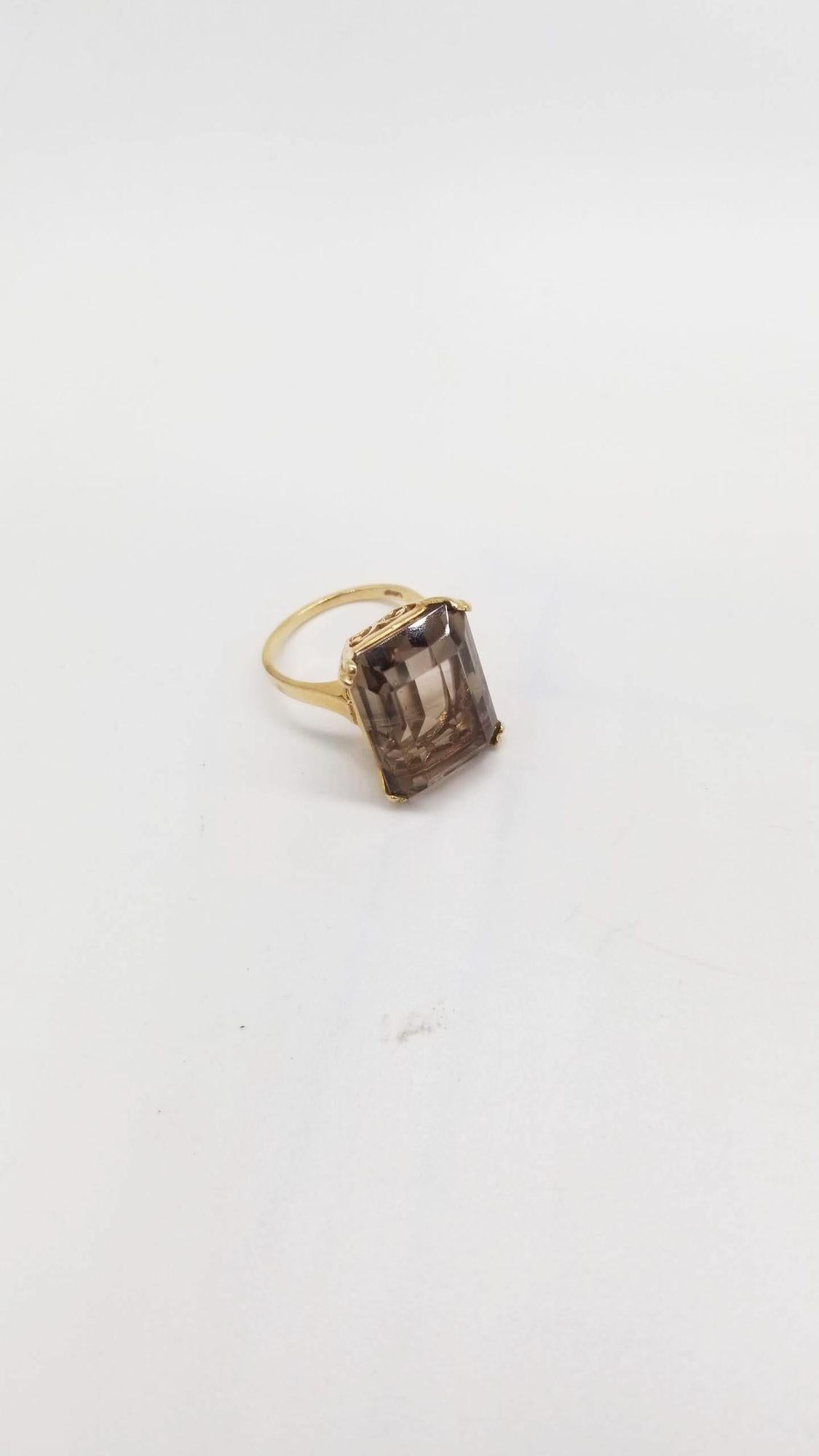 Transport yourself to an era of glamour with this Vintage 14K Yellow Gold Emerald-Cut Smoky Quartz Cocktail Ring. Delicately sized at 5, this exquisite piece showcases a mesmerizing emerald-cut smoky quartz gemstone set in warm, lustrous 14K yellow