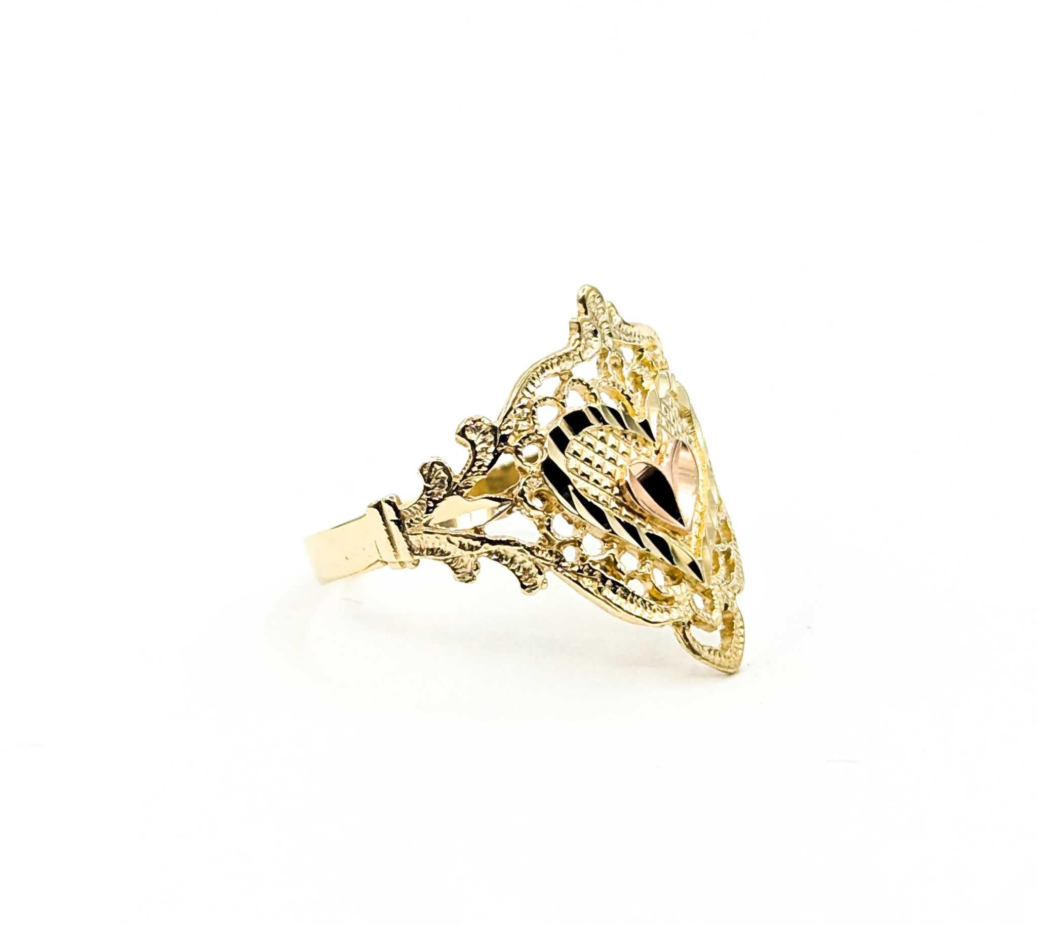 This charming vintage ring is a beautiful example of intricate craftsmanship, featuring a delicate openwork filigree design adorned with a raised heart motif at its center. Crafted in warm 14k yellow gold, the airy latticework showcases fine