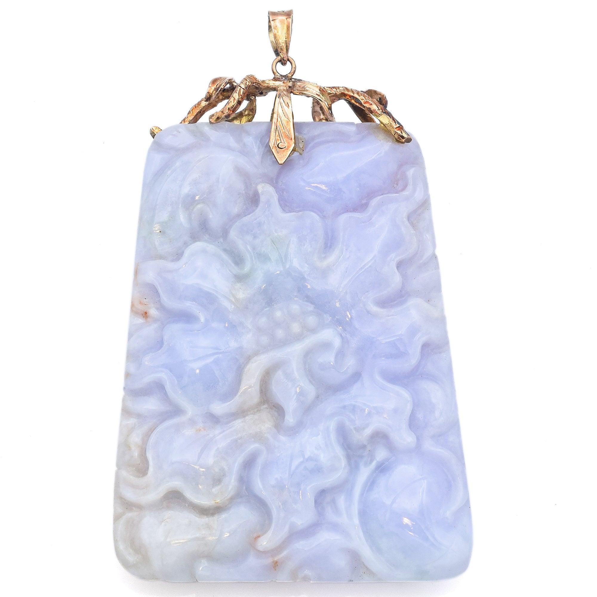 A striking vintage pendant showcasing an intricately carved lavender jade plaque. The jade is richly detailed with floral and squash fruit motifs, symbolizing prosperity and abundance. Its soft lavender hue carries natural variations that add depth