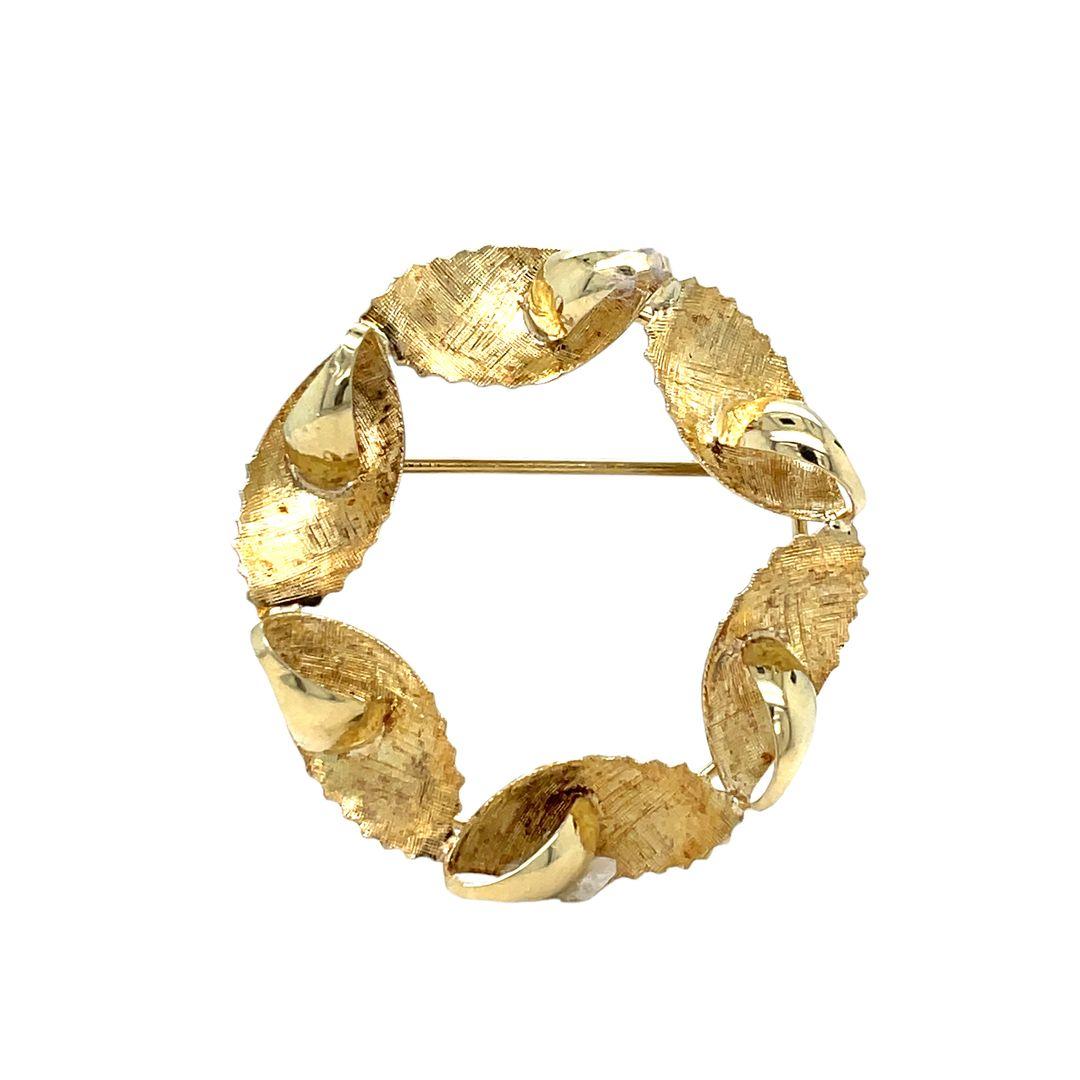 A charming vintage 14K yellow gold brooch showcases a wreath design with finely detailed and textured leaves. The design has a wonderful Florentine finish and the tips of the petals are elegantly curved and high polished, giving it a charming and