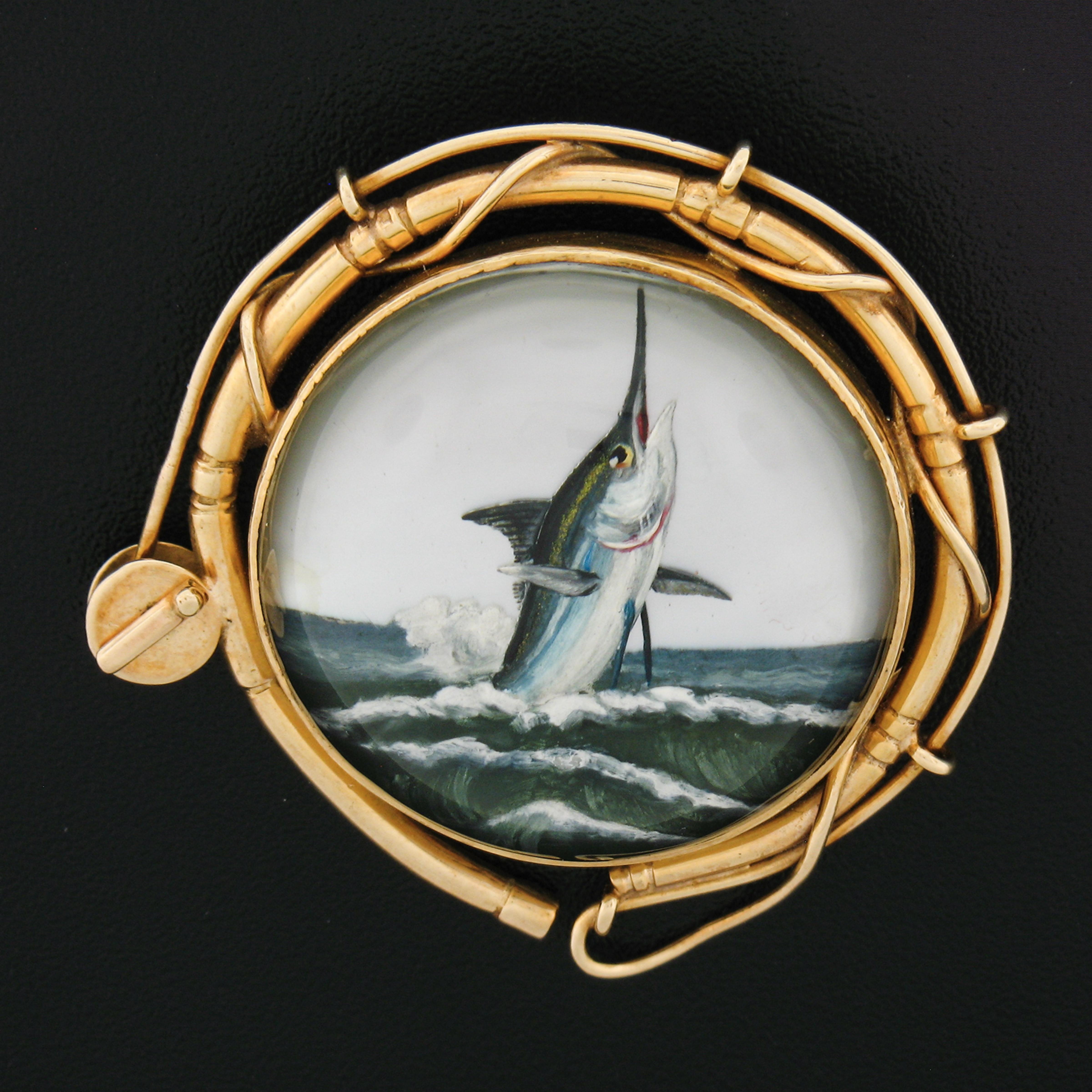 This magnificent vintage brooch was crafted from solid 14k yellow gold. It features an incredibly detailed reverse intaglio of a Marlin fish coming out of the water. The frame features an outstandingly detailed design of a fishing reel surrounding