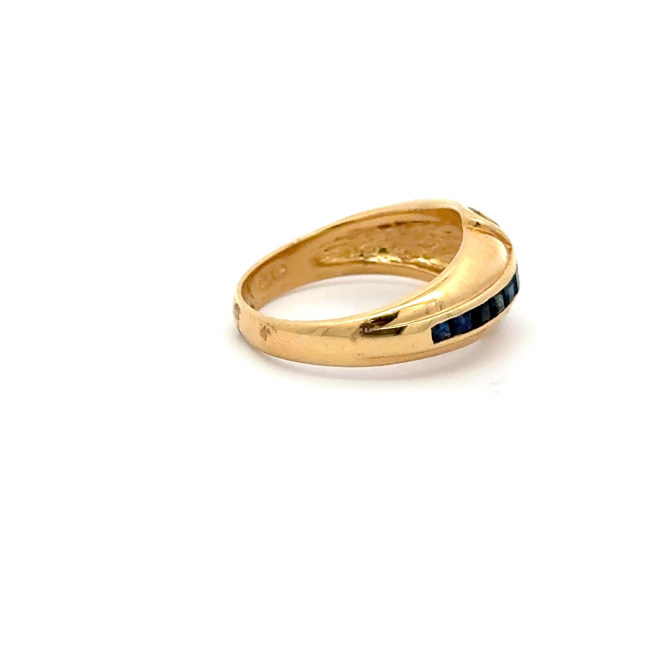 This refined vintage ring crafted in 14K yellow gold features a striking crossover design, elegantly channel-set with deep blue square-cut sapphires (approx. 0.20 carats) and accentuated with a delicate curve of sparkling round diamonds (approx.