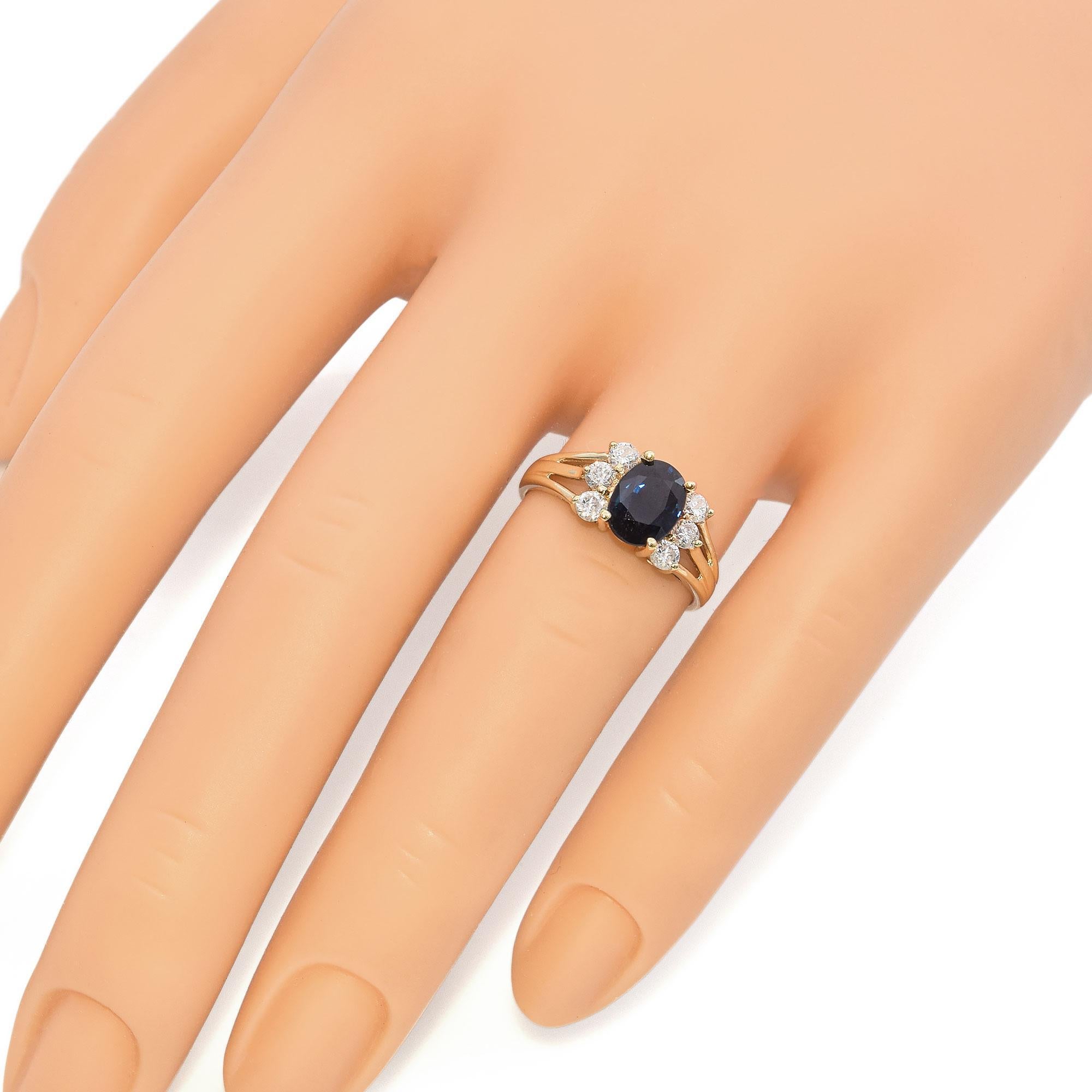 Elegant ring featuring a striking oval blue sapphire at its center, surrounded by a cluster of sparkling round diamonds. The sapphire is securely set in a warm gold band, which splits into a delicate design, enhancing the overall elegance of the