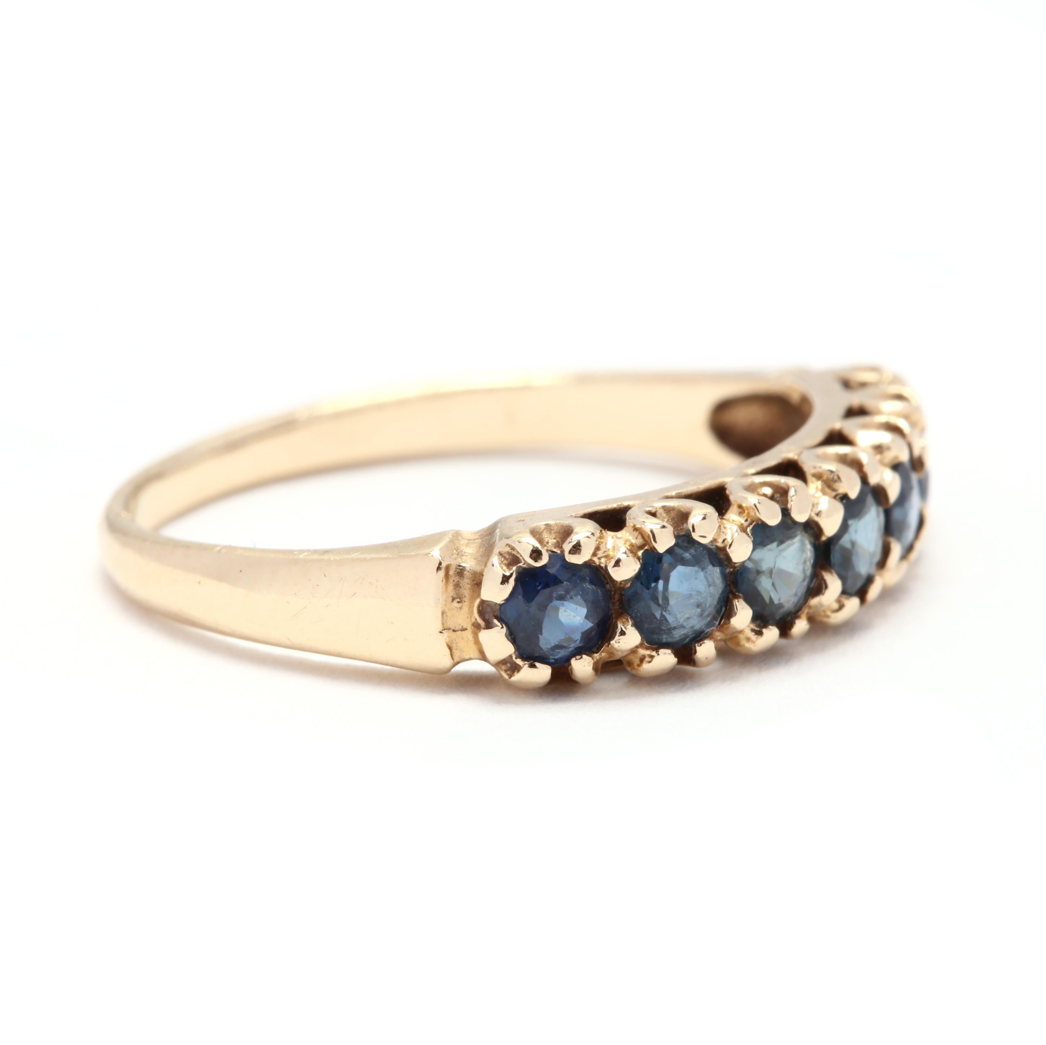 A vintage 14 karat yellow gold and sapphire stackable band ring. This ring features a vintage style seven stone band ring set with round cut sapphires weighing approximately .85 total carats and a slightly tapered shank.

Stones:
- sapphires
- round