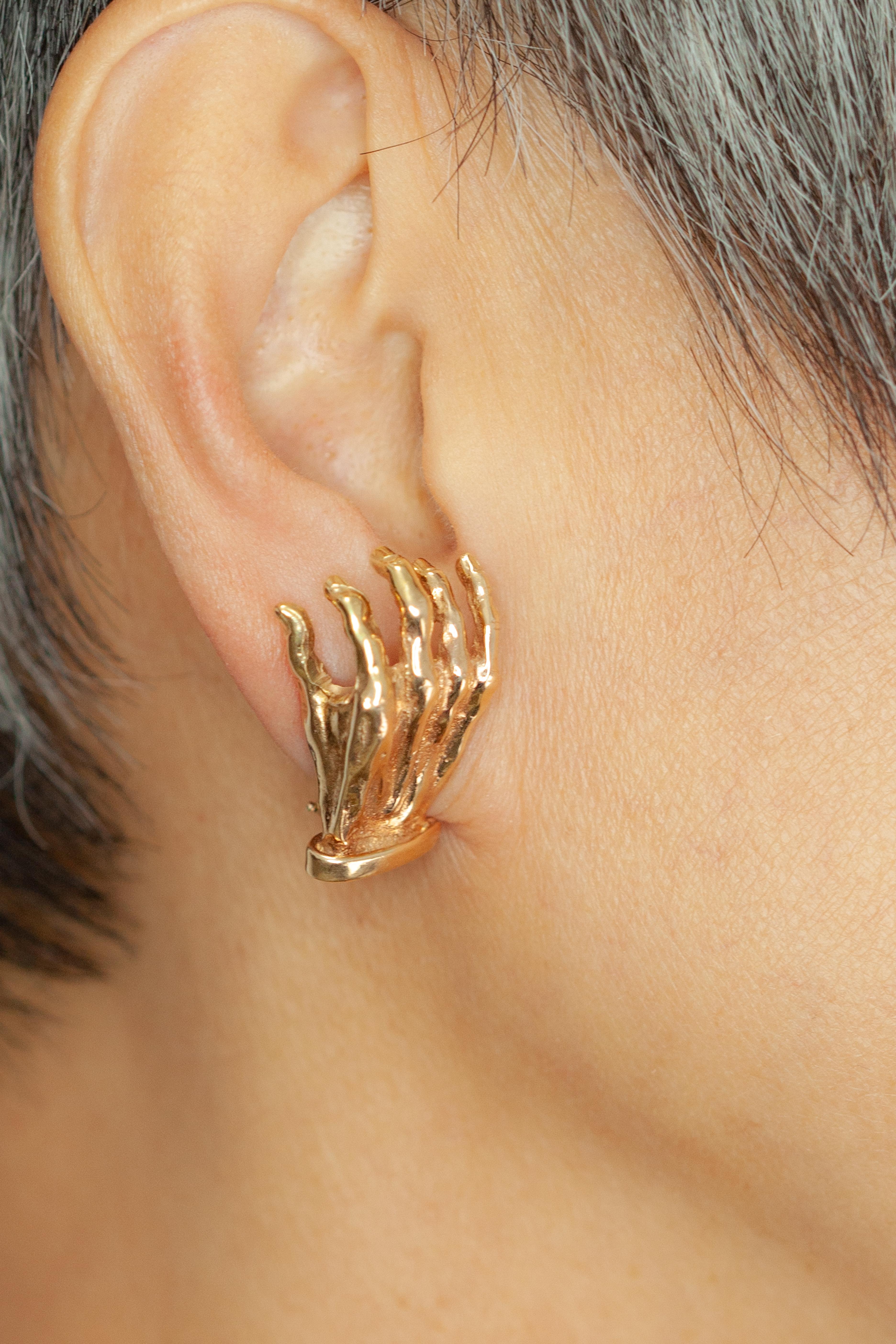 These unique 14K yellow gold earrings, meticulously crafted in the form of sculptural hands. Each earring is modeled in a realistic, open-hand design, capturing expressive detail and texture in high-polish gold. The surrealist aesthetic adds an