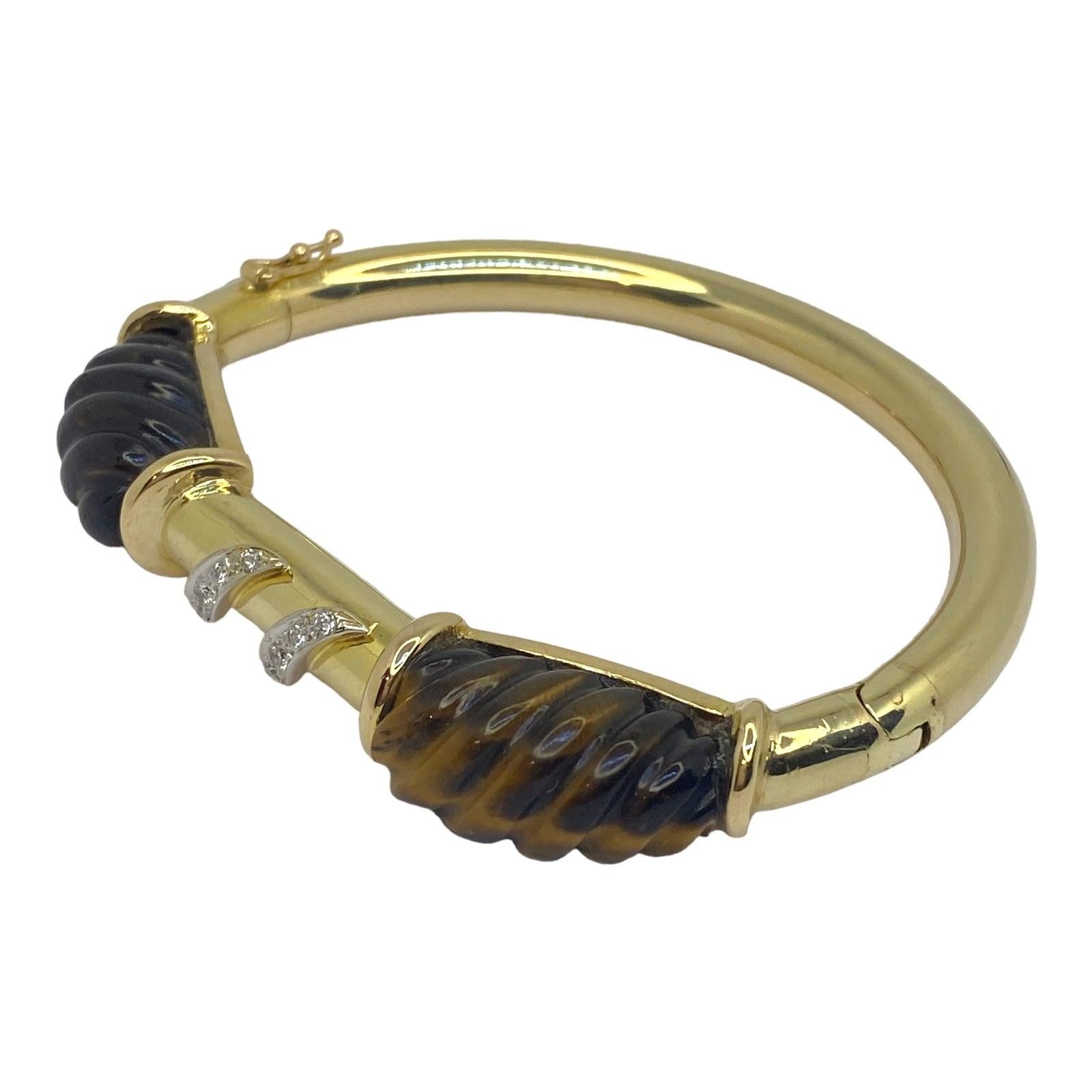Vintage 14K yellow gold hinged bangle bracelet, featuring a tube design set with hand carved fluted tiger's eye gemstones framing two diamond set ribbons on the front. 
10 round brilliant cut diamonds: 0.25 ctw. Color: G-H, Clarity: