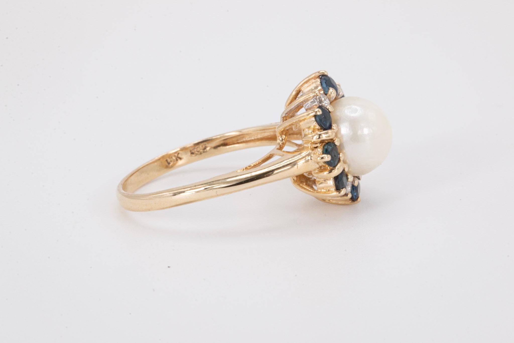 Vintage 14k Gelbgold Weiß Perle, Saphir und Diamant Ring

Ein raffinierter und femininer Vintage-Cocktailring aus massivem 14-karätigem Gold mit einer leuchtenden weißen Naturperle, die von funkelnden Diamanten und tiefblauen Saphiren akzentuiert