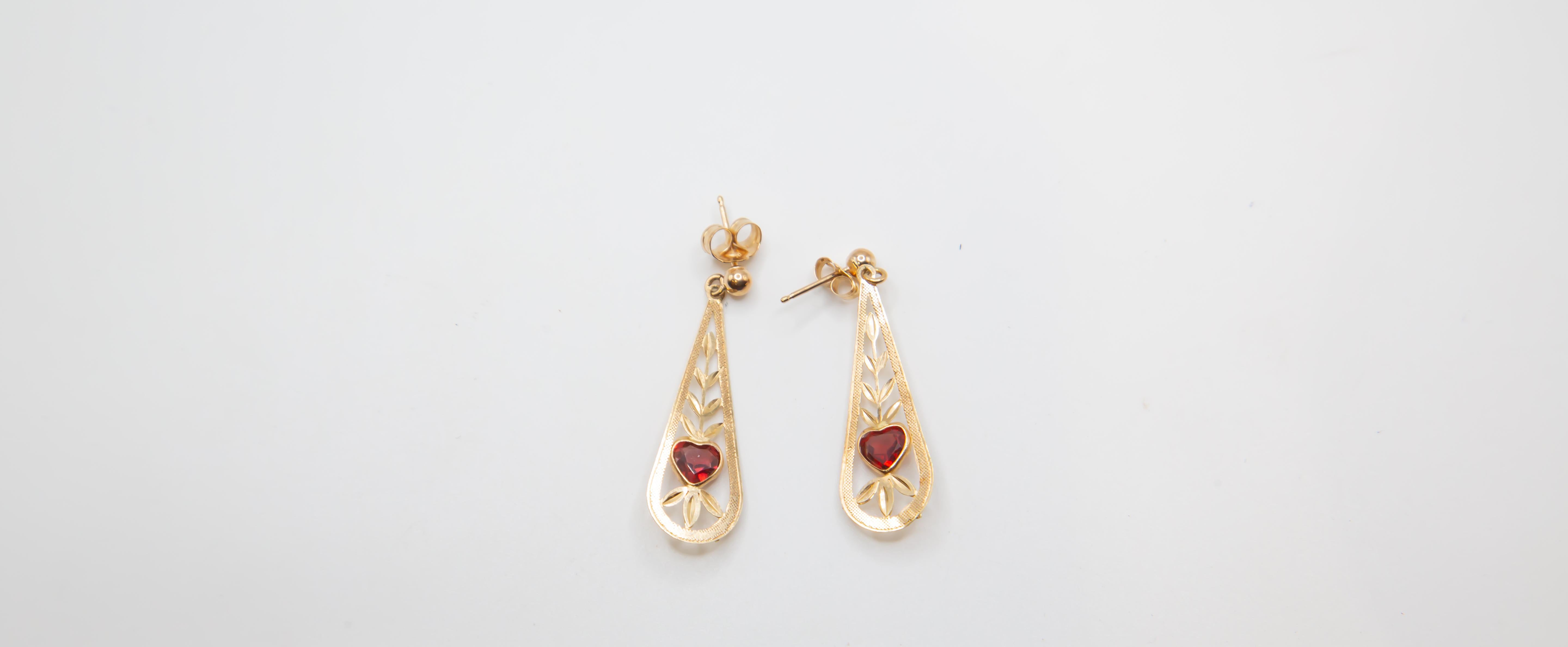 Ein zartes und romantisches Paar Ohrringe aus 14-karätigem Gold mit durchbrochenem Filigran mit stilisiertem Blattmotiv und lebhaften herzförmigen Granatsteinen in der Mitte. Das längliche Tropfen-Design umrahmt anmutig die tiefroten Edelsteine und