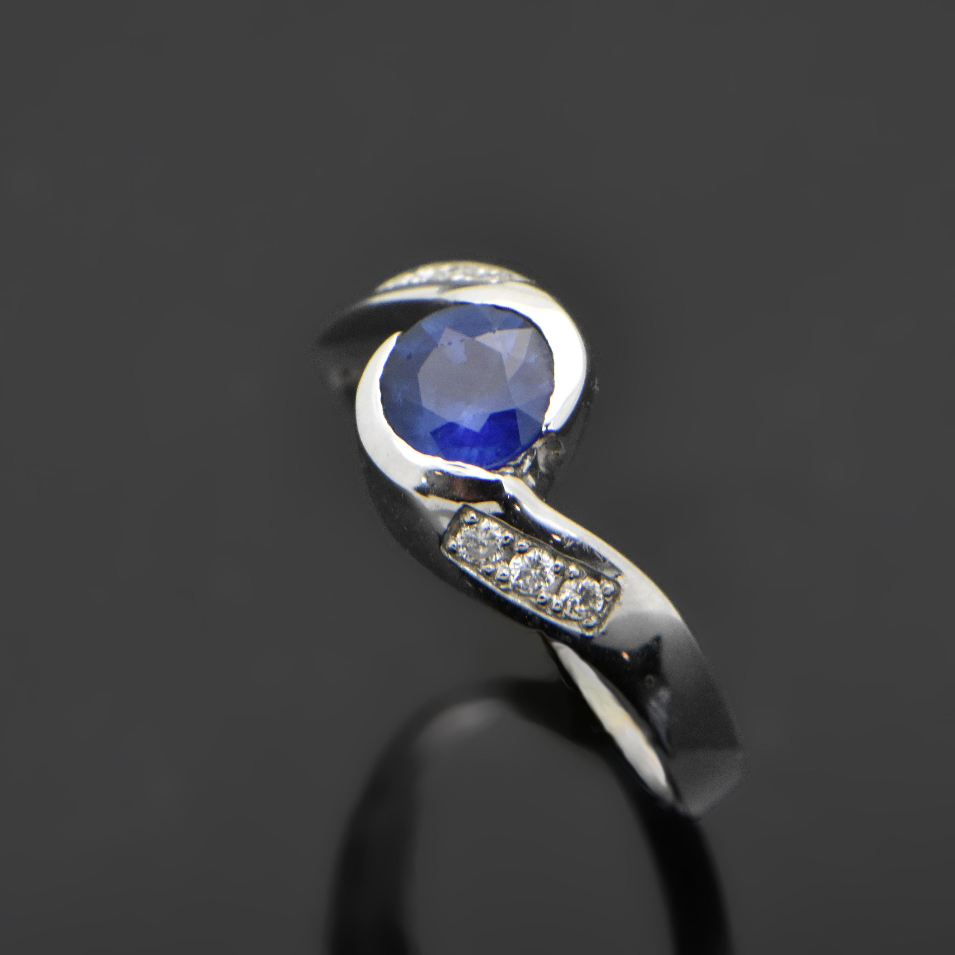 This unique ring is a vintage 14kt white gold setting featuring a round sapphire with an estimated weight 0.67 and 3 diamonds on each shoulder with an estimated 0.06 cttw. Estimated weight of gold is 2 gr. 
We will size it for you.

