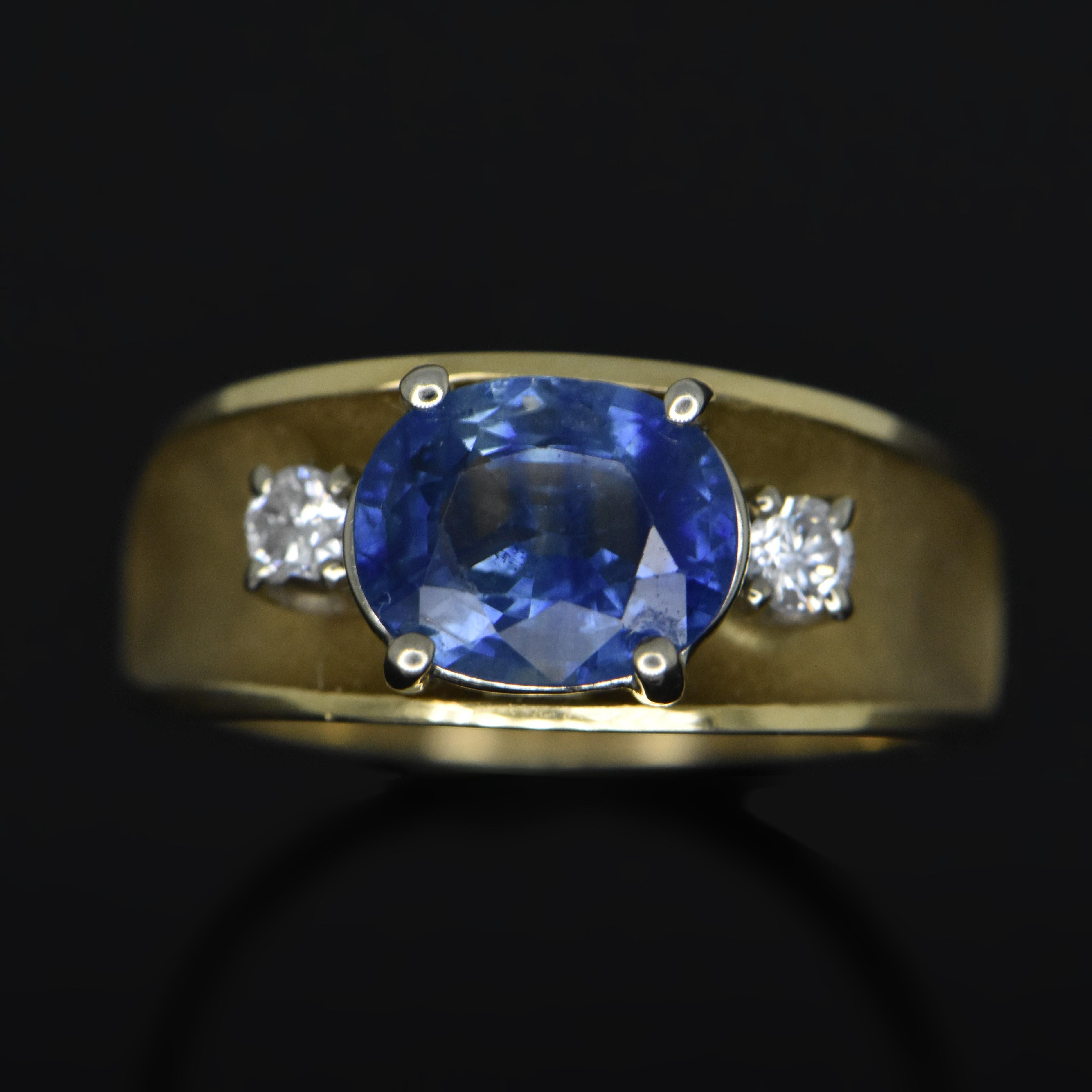 A vintage 14kt yellow gold ring featuring a stunning oval-cut blue sapphire with an estimated weight of 1.19ct. and two side diamonds at 0.16 cttw. on a wide band. Estimated weight of gold 3.5 gr. 

We will size it for you. 


