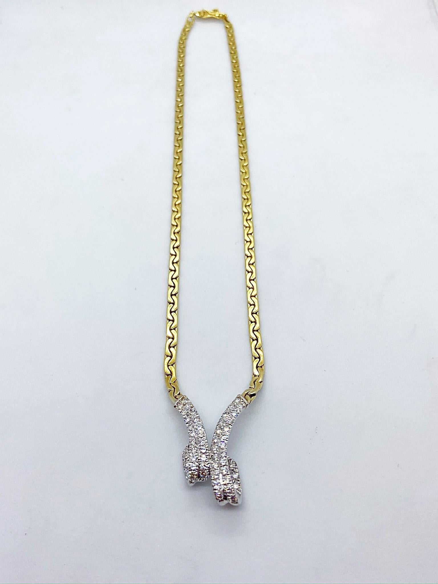 This 14 karat gold necklace is designed with a white gold center ribbon like section set with round Brilliant Diamonds. The yellow gold chain is a flat c link. The total length of the necklace measures 15.5