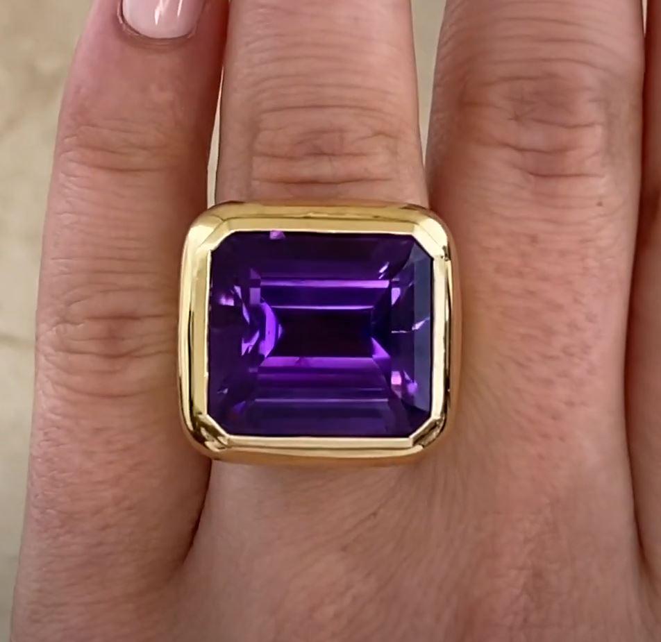 This exquisite vintage cocktail ring showcases a stunning emerald-cut amethyst, approximately 15-carats in weight, as its centerpiece. The vibrant purple hue of the amethyst is beautifully complemented by its bezel setting, which enhances the