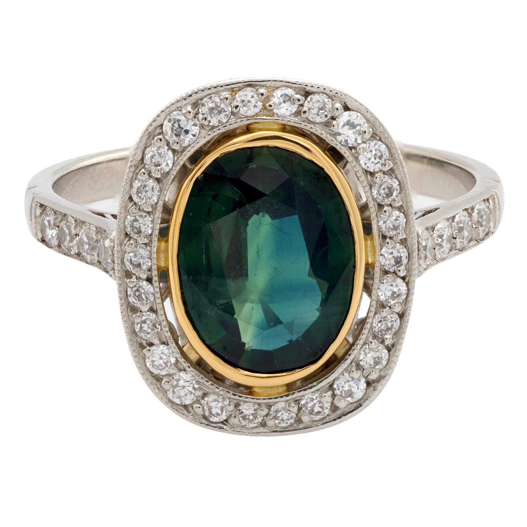 Dieser Vintage-Ring aus 18 Karat Gelbgold und Platin aus den 1990er Jahren präsentiert einen grünen Saphir mit 1,60 Karat im Ovalschliff, der von vierunddreißig Diamanten im alten europäischen Schliff von insgesamt etwa 0,30 Karat in der Farbe F-G