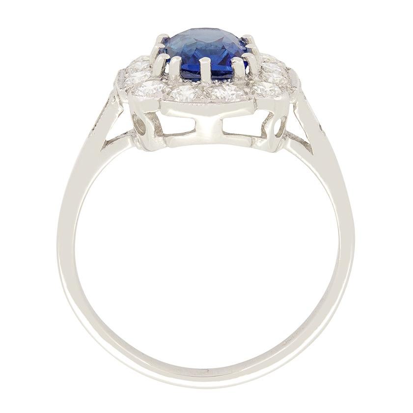 This beautiful vintage cluster ring features a delightful sapphire surrounded by a halo of round brilliant diamonds.  The cushion cut sapphire has a carat weight of 1.60 carat and is claw set into platinum. The diamonds total 0.60 carat are are of