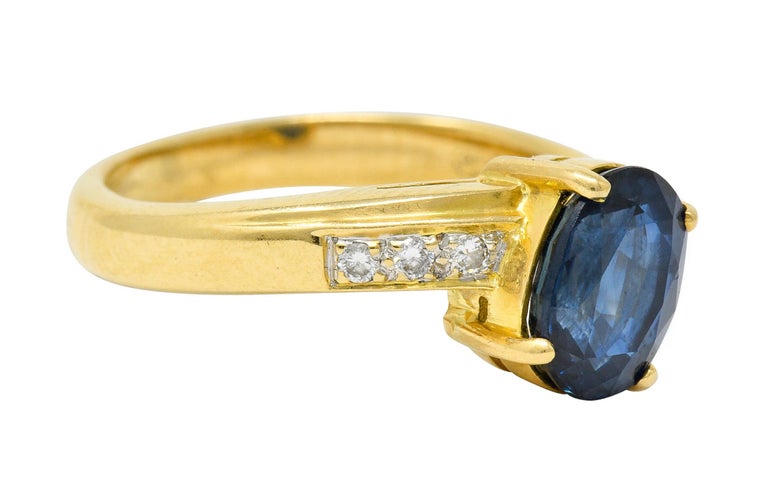 Bypass style ring centering an oval cut sapphire weighing approximately 1.51 carats

Transparent and medium-dark blue in color

Flanked by round brilliant cut diamonds weighing approximately 0.10 carat; eye-clean and white

Stamped 750 for 18 karat