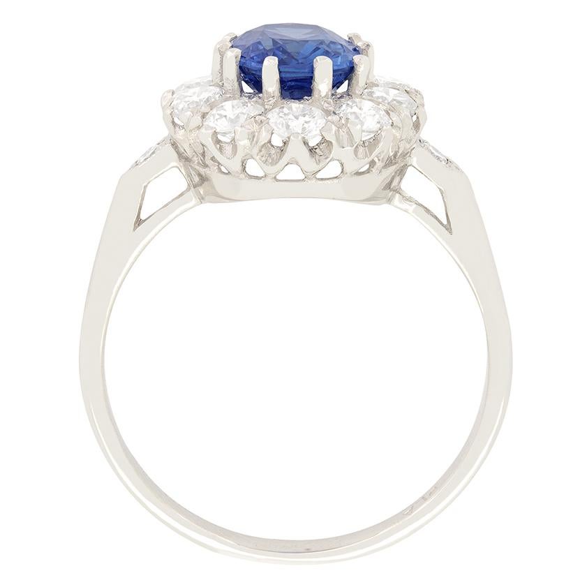 An impressive 1.70 carat sapphire sits amongst a cluster of round brilliant diamonds in this vintage cluster ring from the 1970s. The oval cut sapphire has a beautiful mid blue tone which, set amongst the whiteness of the diamond stands out