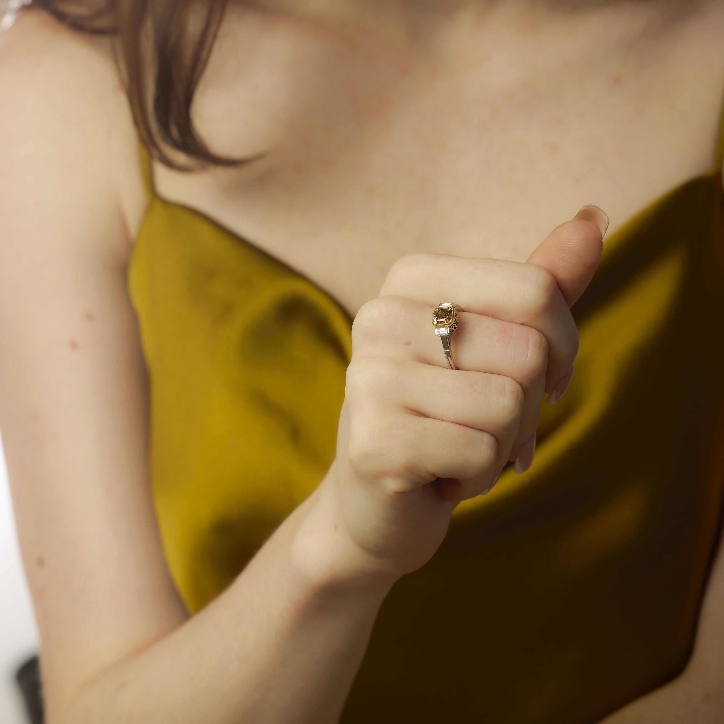 This vintage ring from the 1990s showcases a striking 1.75 carat fancy yellow brown Asscher cut diamond, its bold hue and clean facets radiating distinctive brilliance. Flanked by two sleek baguette cut diamonds totaling approximately 0.10 carats,