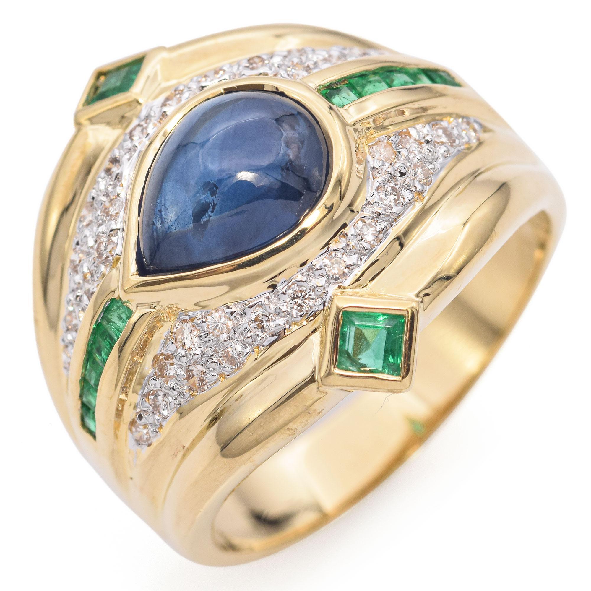 Late 20th Century Yellow Gold Sapphire Emerald Diamond Ring. The centerpiece features a captivating blue cabochon-cut sapphire, surrounded by an arrangement of diamonds. Accentuating the design are vibrant green emerald-cut emeralds. The ring offers
