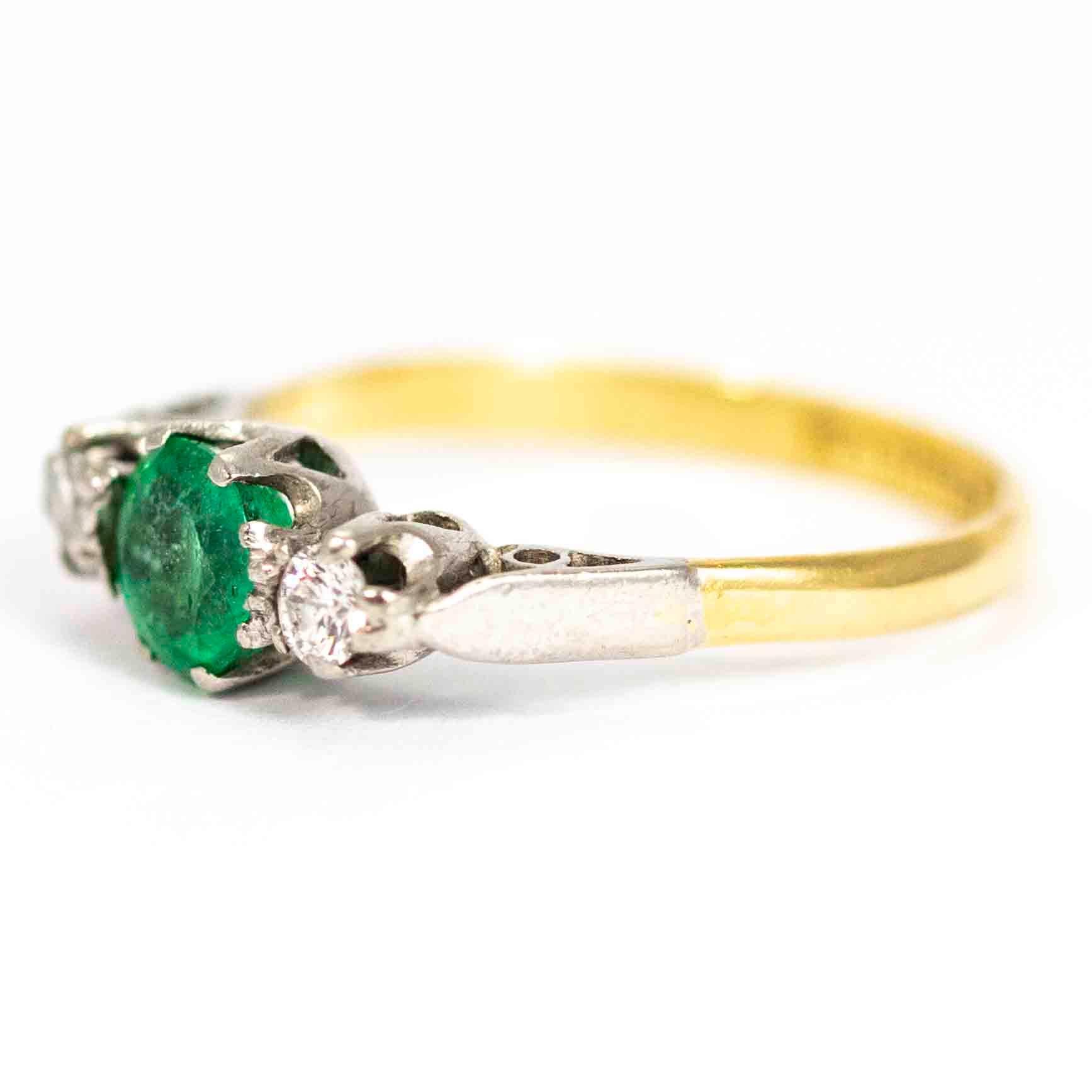 A wonderful vintage three-stone ring. Centrally set with a stunning round emerald measuring approximately 70 points, flanked either side by 10 point round cut diamonds. The stones and shoulders are set in platinum, the band is modelled in 18 carat