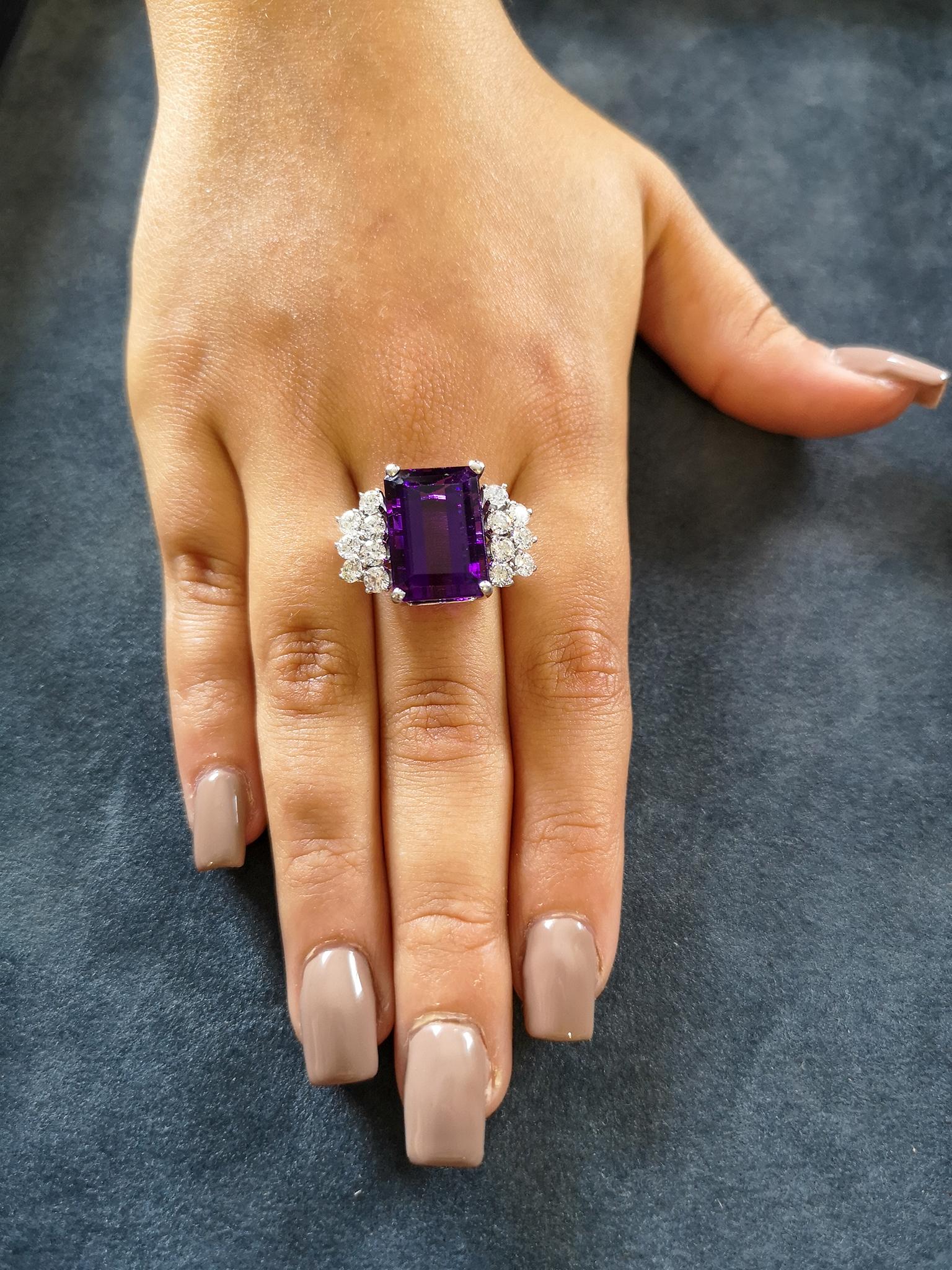 An exquisite, vibrant cocktail ring, featuring an emerald cut amethyst of deep, regal purple, weighing approximately 12 carats, flanked on each side by a cluster of seven brilliant-cut diamonds, totaling approximately 1.50 carats, H-I colour and VS