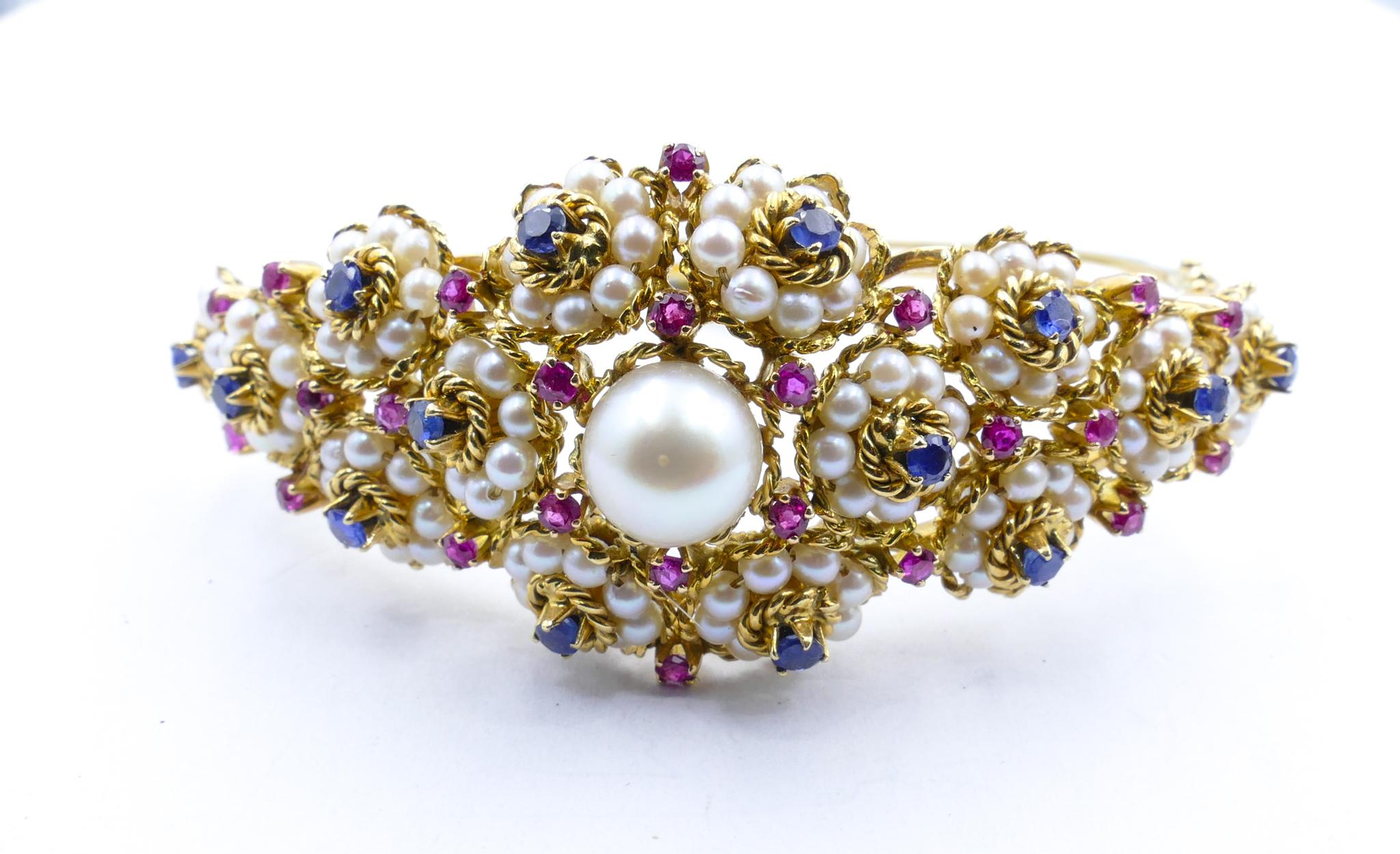 What a beautiful and unique bangle. 
Featuring a gorgeous floral design the Centrepiece of which is a largeish creamy Pearl of very good lustre.
This is surrounded by over 1.6 carats of deeply hued blue and vivid pink Sapphires  claw set in a