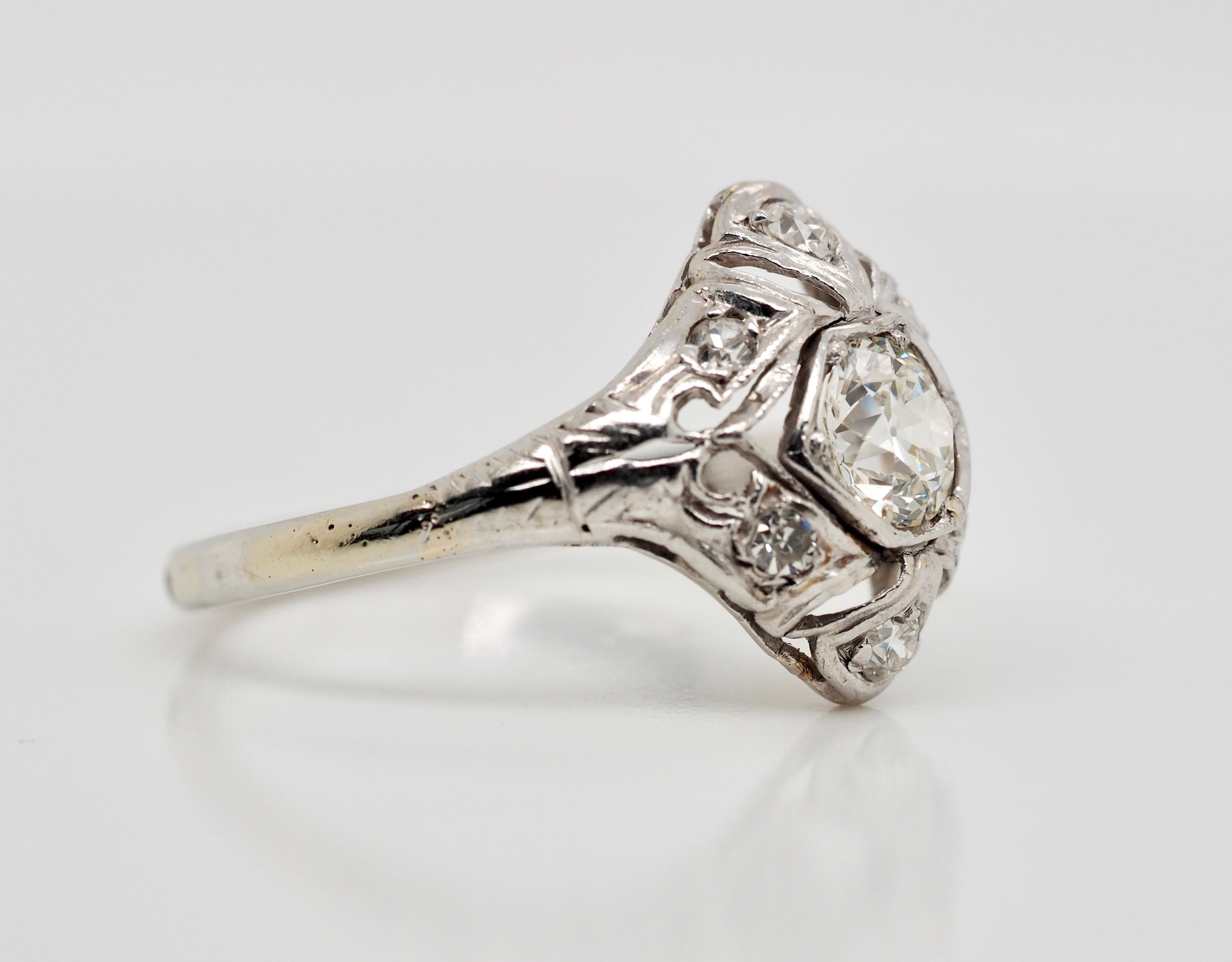 This Vintage Art Deco Ring is crafted in 18K white gold and dates back to the 1920's. The brilliant center diamond is a 0.70 carat old European cut, H Color VS2 clarity. There are 6 accenting European cut diamonds set around the center stone