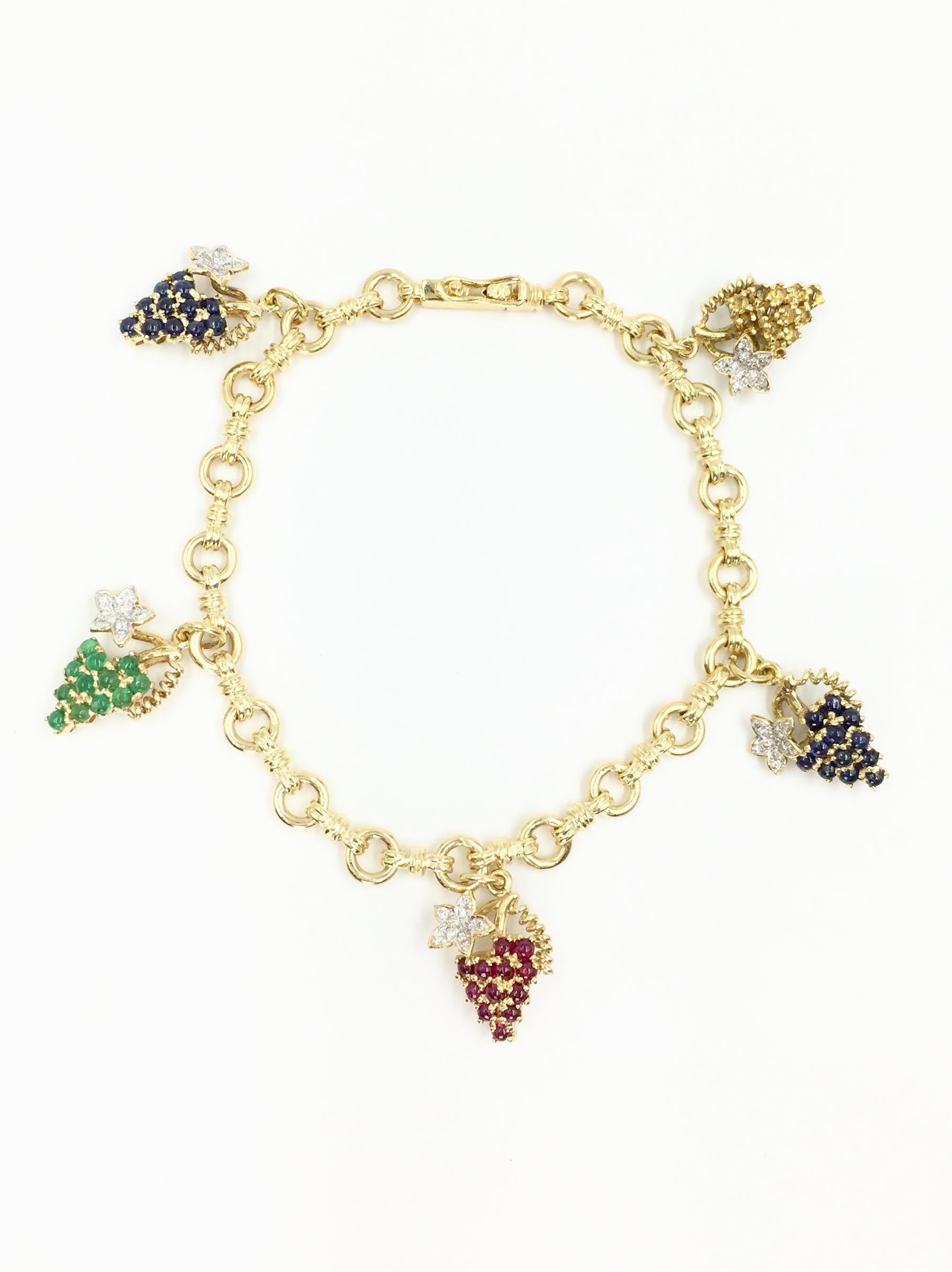 18 Karat solid gold linked charm bracelet featuring five diamond and precious gemstone dangling grape charms. Charms have a total weight of .21 carats of diamonds at approximately F color, VS2 clarity. 1.40 carats of blue sapphires, 1.06 carats of