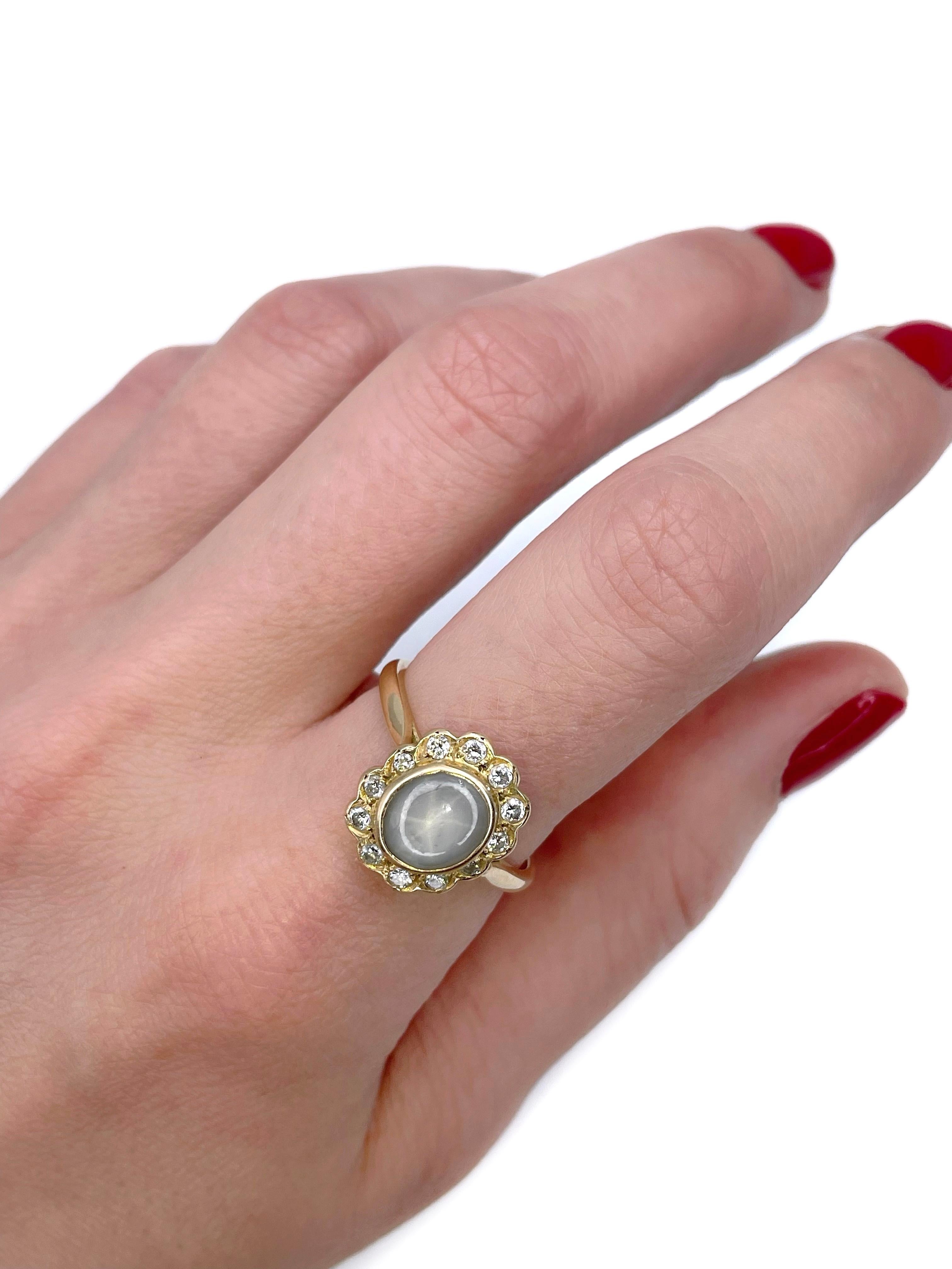 Dies ist ein außergewöhnlicher Vintage-Cluster-Ring in 18K Gold gefertigt. Circa 1980. 

Er verfügt über folgende Merkmale:
- 1 Sternsaphir (ovaler Cabochon-Schliff, 2,30ct, graue Farbe, deklassiert)
- 12 Diamanten (runder Brillantschliff, TW