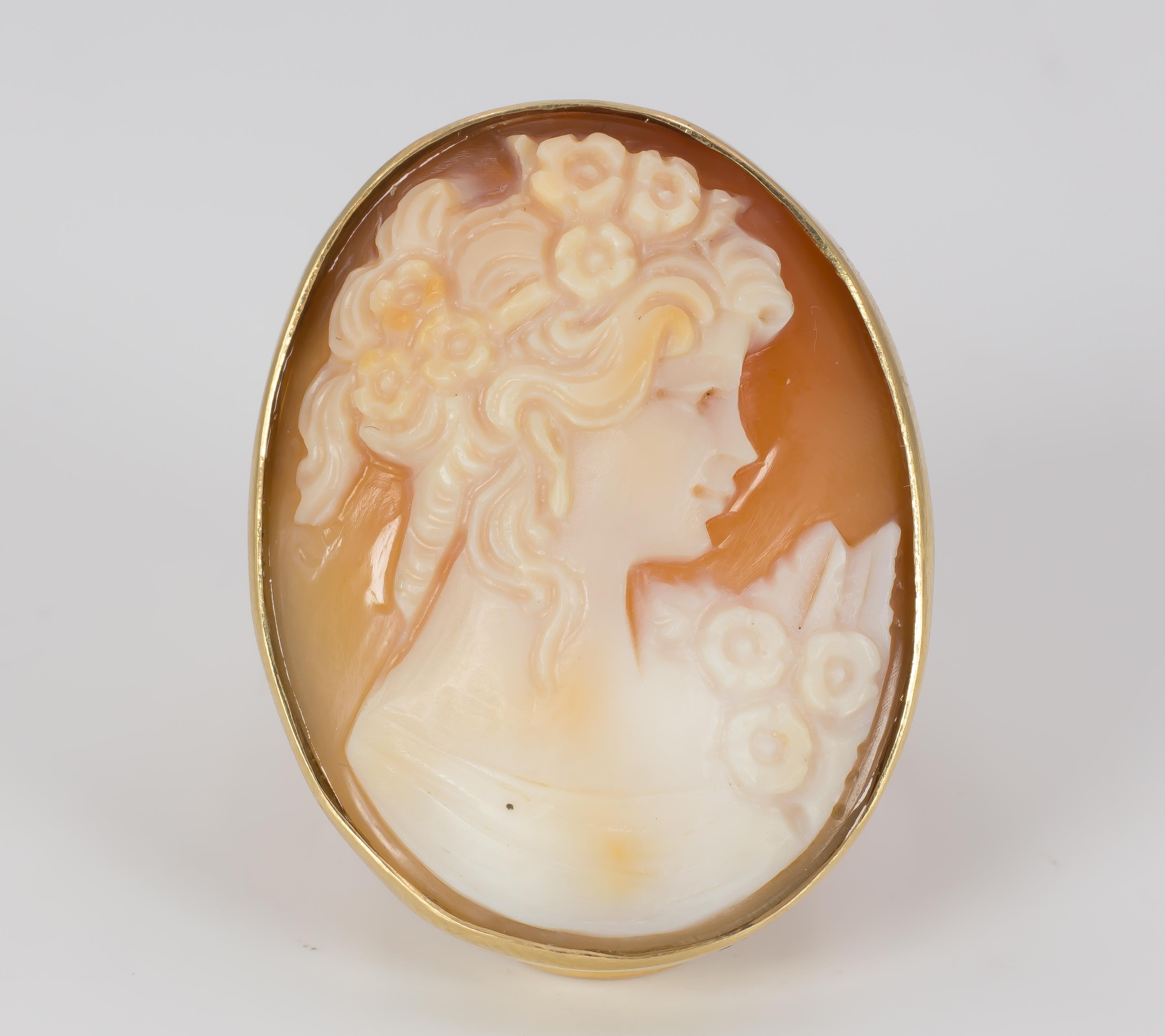 This stunning vintage ring, dating from the 1950s, is set with a central cameo, carved on a shell with a young woman profile: she is really beautiful, with collected and wavy hair, decorated with some flowers; some of them are placed also on the