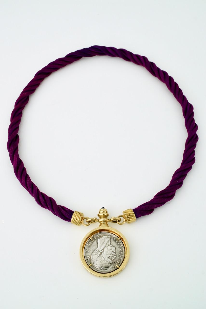 A vintage gold silver and cord coin necklace featuring an Italian silver 1928 silver 10 lire coin set in a gold mount with a sapphire terminal and mounted with a purple twisted cord with 18k yellow gold fluted caps attached with hinged clasps to the