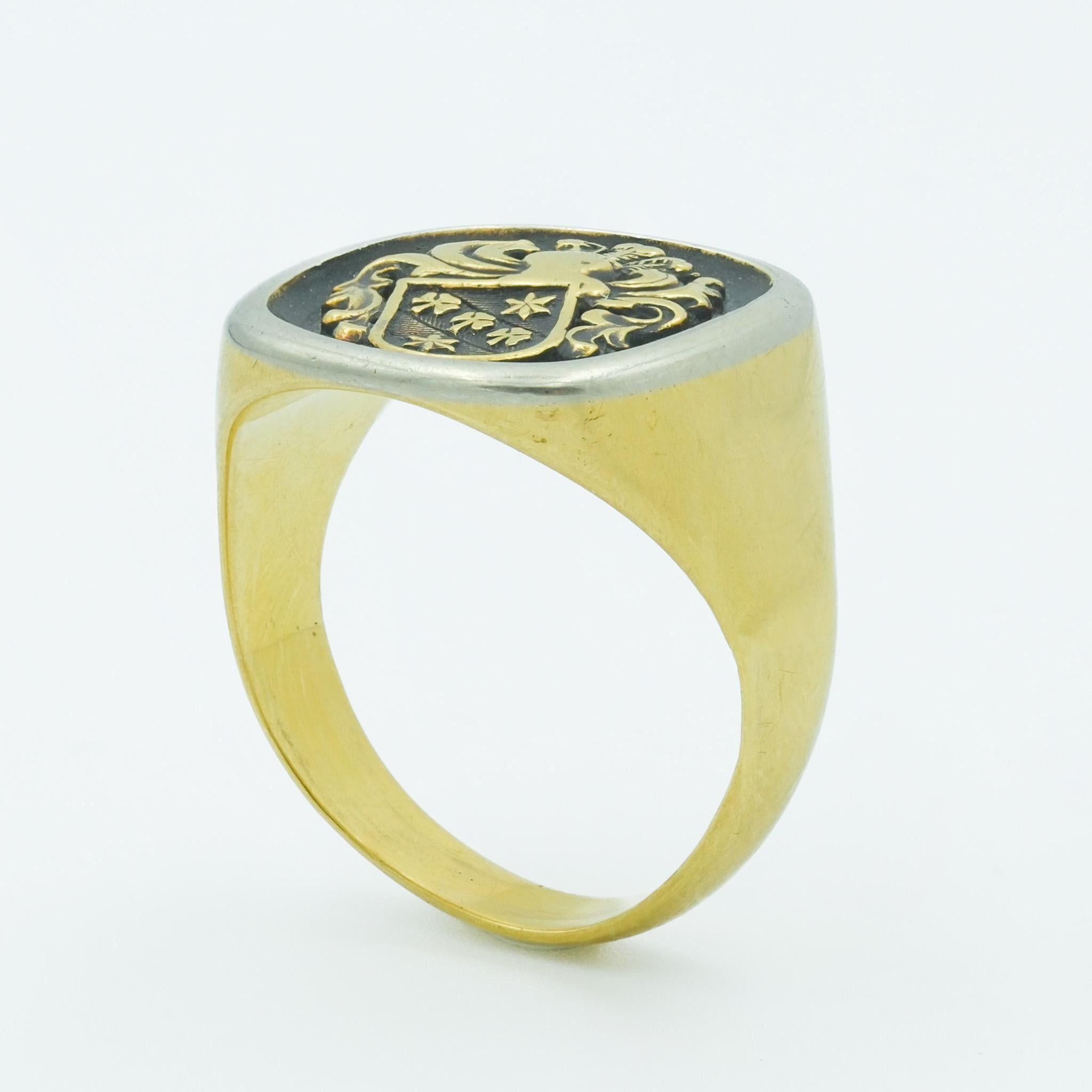 This vintage 18 karat yellow and silver accent signet ring is emblematic of historical significance and personal identity. The centerpiece is a crest, meticulously engraved and filled with a likely resin-based black ink or paint, which in times past