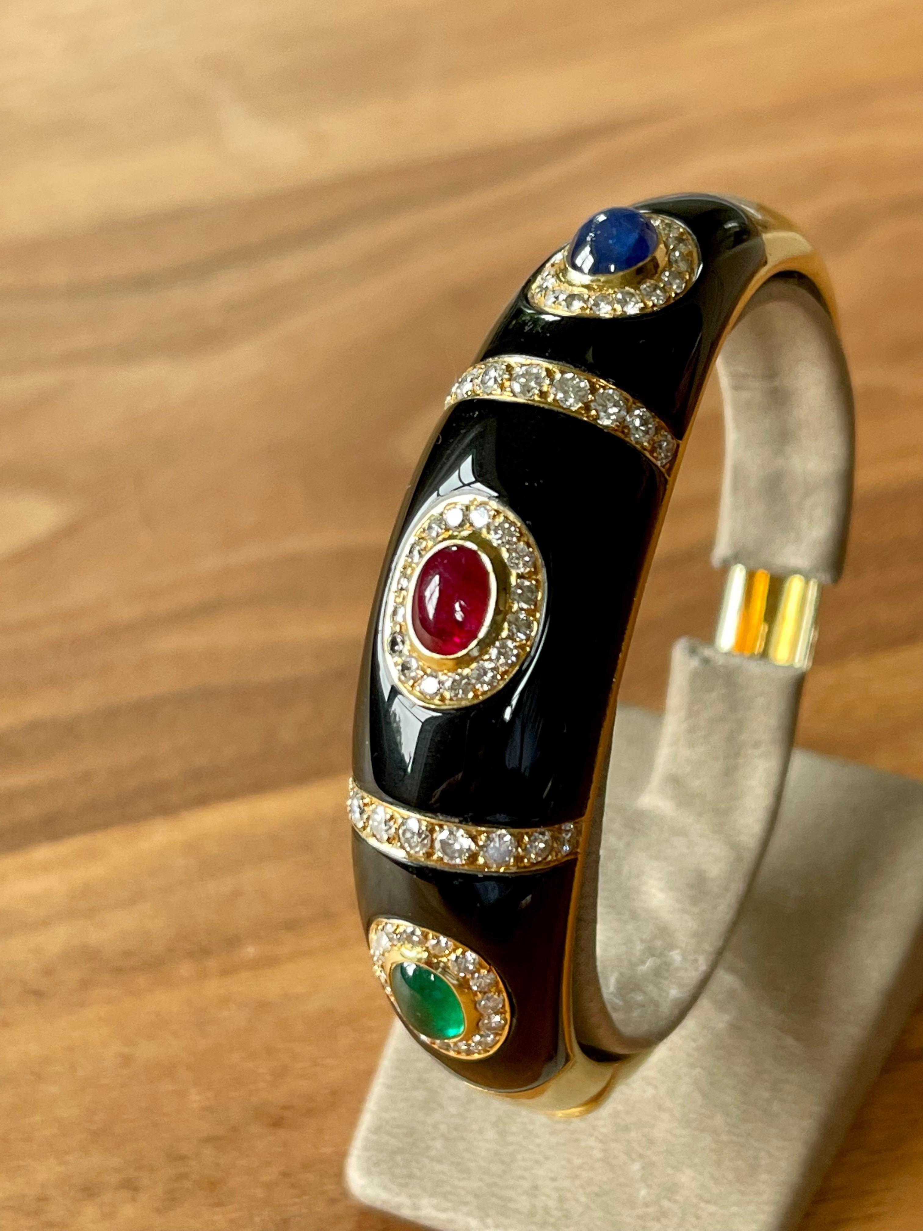 Bracelet élégant des années 1980 en or jaune 18 K avec émail noir, cabochon de rubis, de saphir et d'émeraude accentué par 75 diamants de taille brillant pesant environ 1,80 ct. Diamètre au point le plus large 6 cm. 
Toutes les femmes seront