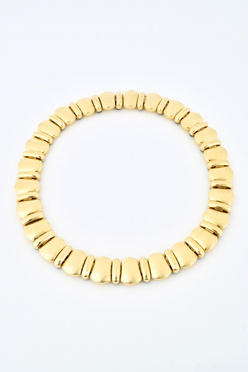 A vintage necklace of 25 flared puffy pillow shaped panels of 18k yellow gold interspersed with long lozenge shaped cabochons of deep blue Lapis Lazuli bezel set and finished with an integrated push clasp; the tongue and button of which is in white
