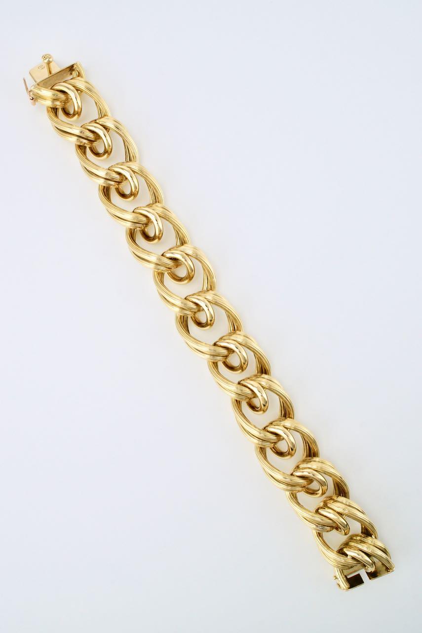 An 18 karat yellow gold bracelet of 12 textured links made up of a fluted double link one of which loops the next group of two links and finished with an integrated box clasp and a figure of eight safety closure - an elegant large scale bracelet