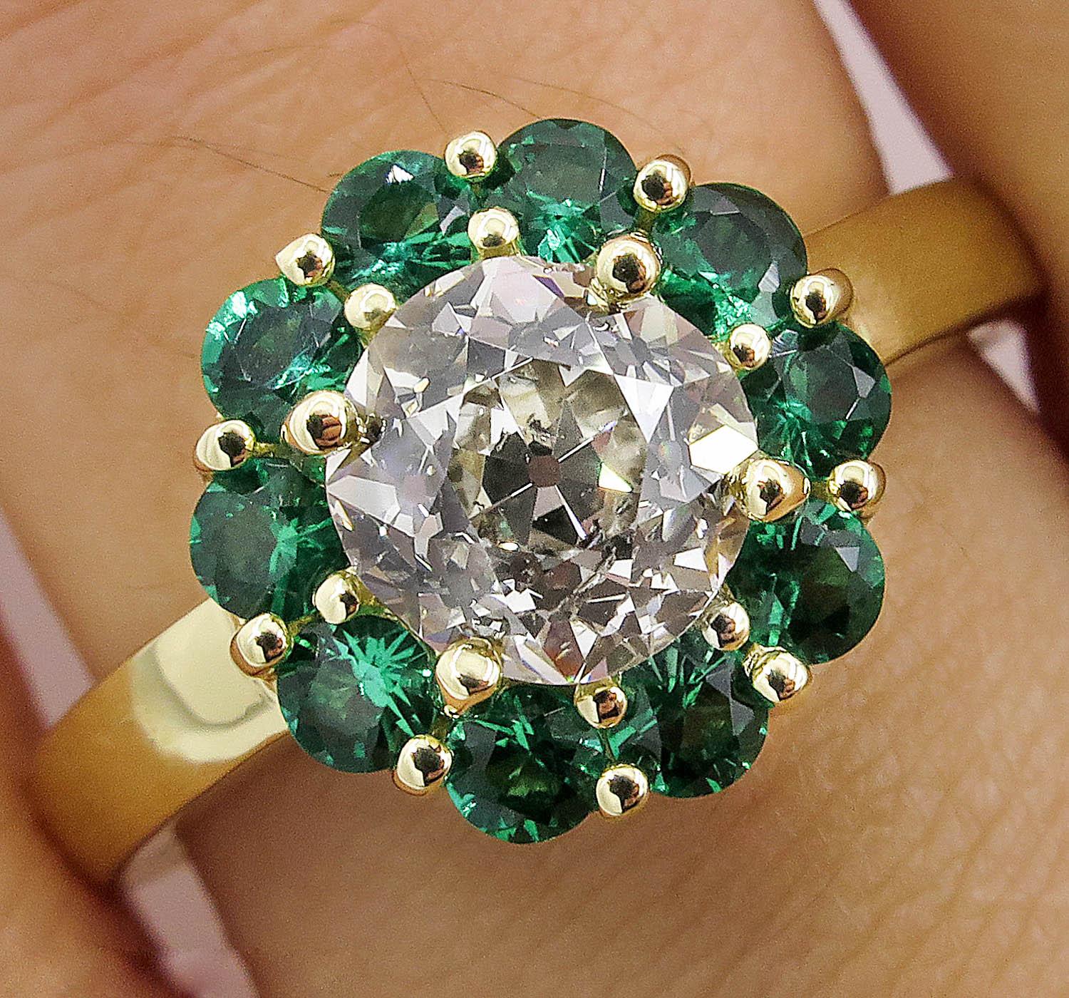An Amazingly beautiful and Delicate Vintage Flower shaped 18k Yellow Gold Ring (stamped); the Center Diamond is Gemologic Certified 1.20ct Old European in K-L Color and SI2 clarity.
It is surrounded by 10 Round shaped NATURAL Bright Green Emeralds;