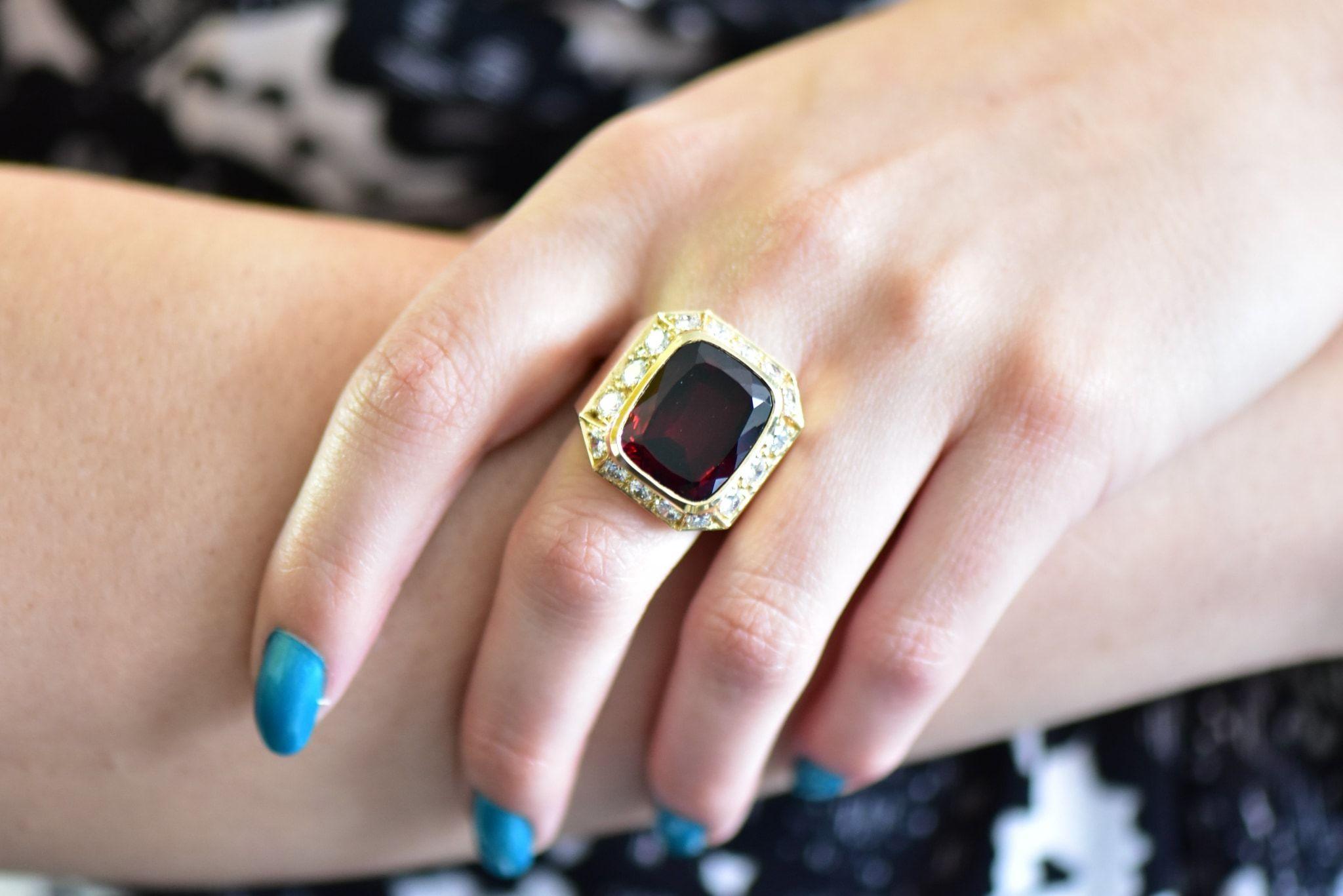 Centering a rectangular cushion cut garnet weighing approximately 18.20 carats, deep intoxicating red color

With a round brilliant cut diamond surround, weighing approximately 2.25 carats total, G color and VS to SI clarity

Vintage design

Ring