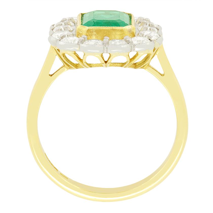Dating to the 1970s, this beautiful cluster ring features a radiant green emerald in the centre. The emerald is a classic oval cut stone weighing 1.85 carat and is rub over set into milgrained 18 carat yellow gold. Surrounding the emerald is a halo