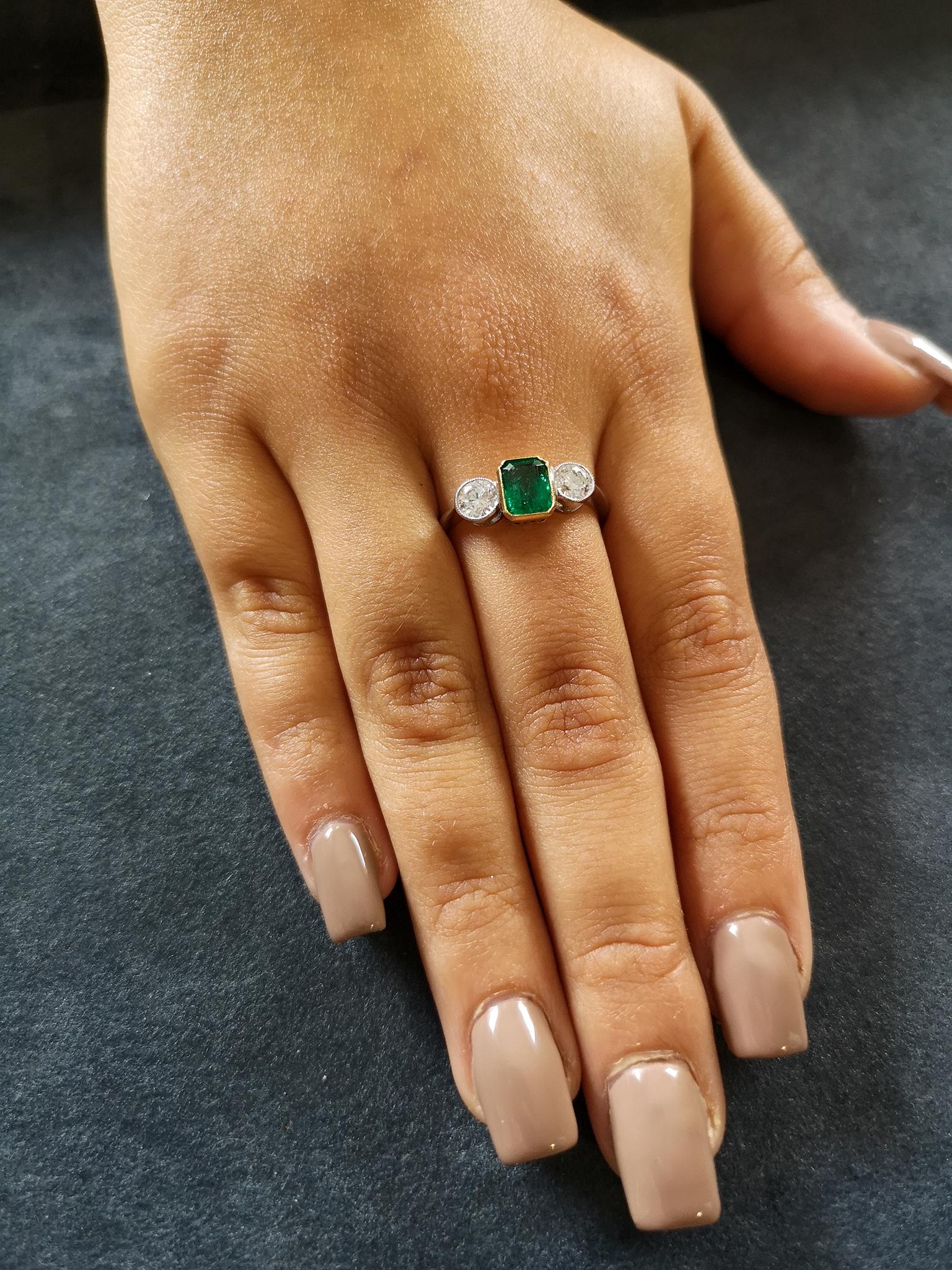 The central emerald-cut emerald of bottle green colour and approximately 1.25 carats mounted in an 18-carat yellow gold bezel setting, flanked on each side by a single brilliant-cut diamond, each approximately 0.40 of a carat, H colour and SI