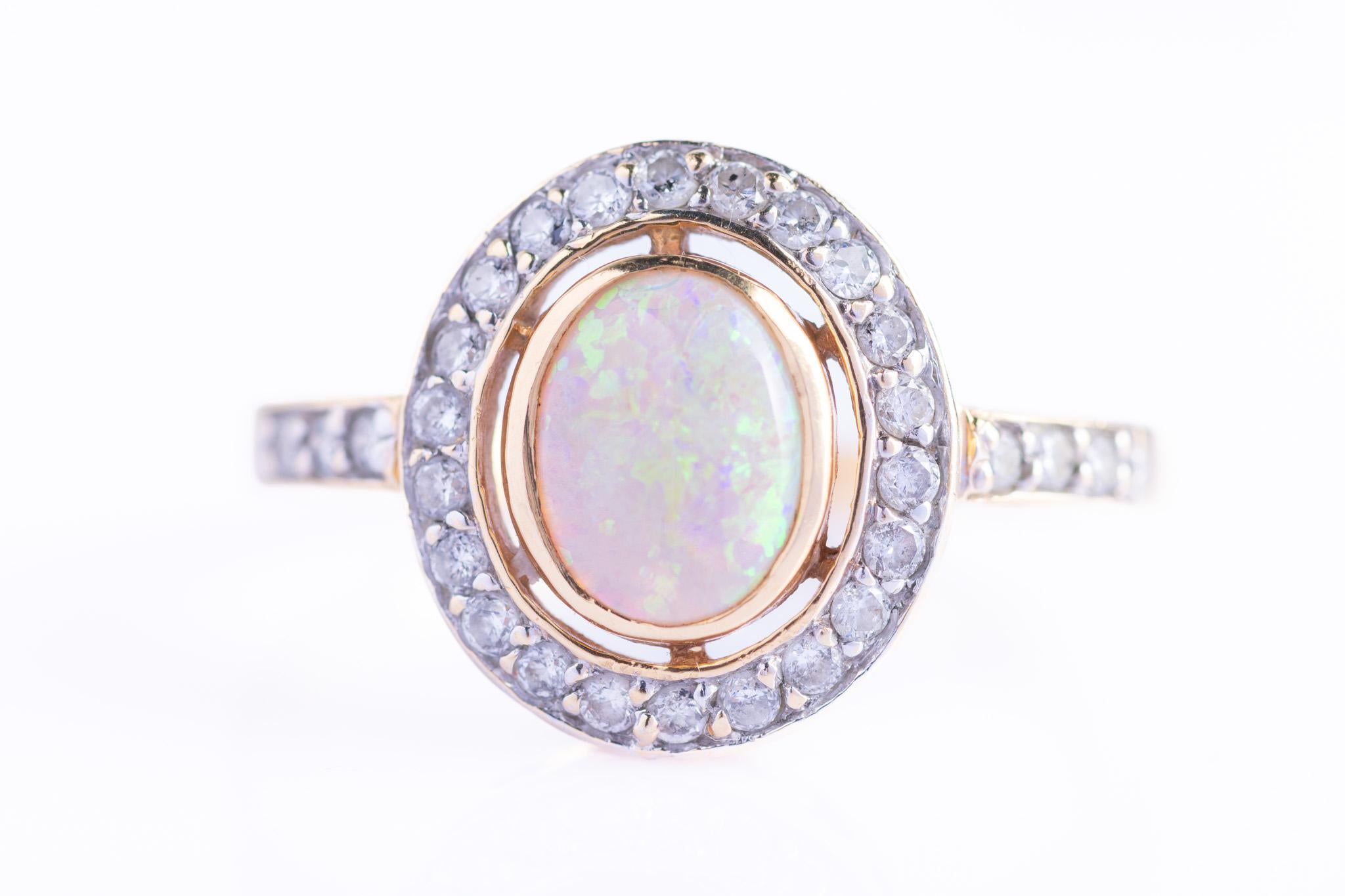 This stunning and luminous opal and diamond cluster ring is set in 18ct yellow gold. The central white opal cabochon shimmers with delicate play-of-colour, encircled by a halo of bright brilliant-cut diamonds set in yellow gold, with further