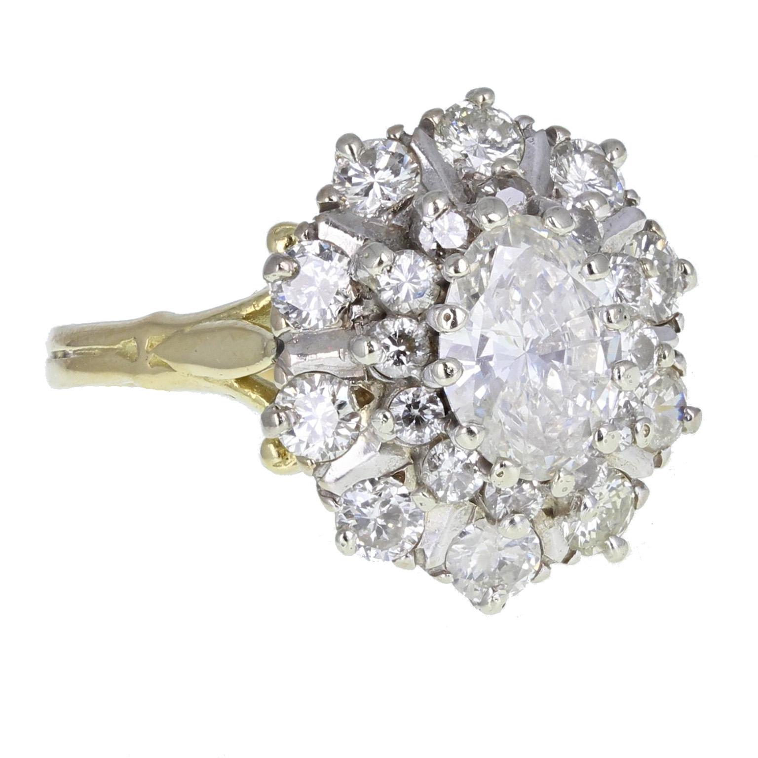 A sparkling and fine quality central oval brilliant-cut diamond mounted in 18-carat white gold claws, surrounded by a halo of 12 melee diamonds, further accented by 10 brilliant-cut diamonds, bar-set to form an oval shaped cluster ring.